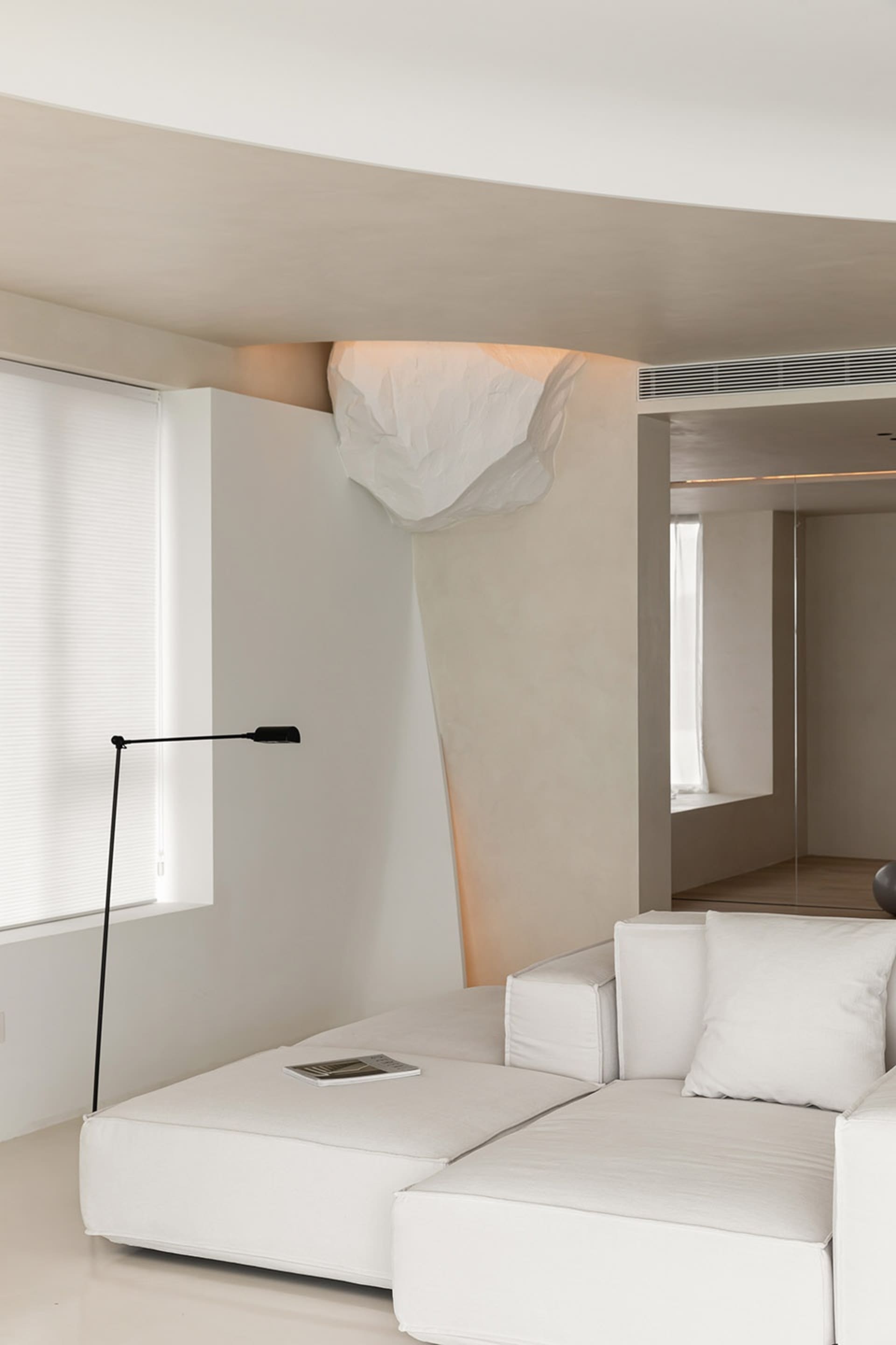 A modern minimalist living room featuring a white sofa, floor lamp, and geometric lighting fixture.
