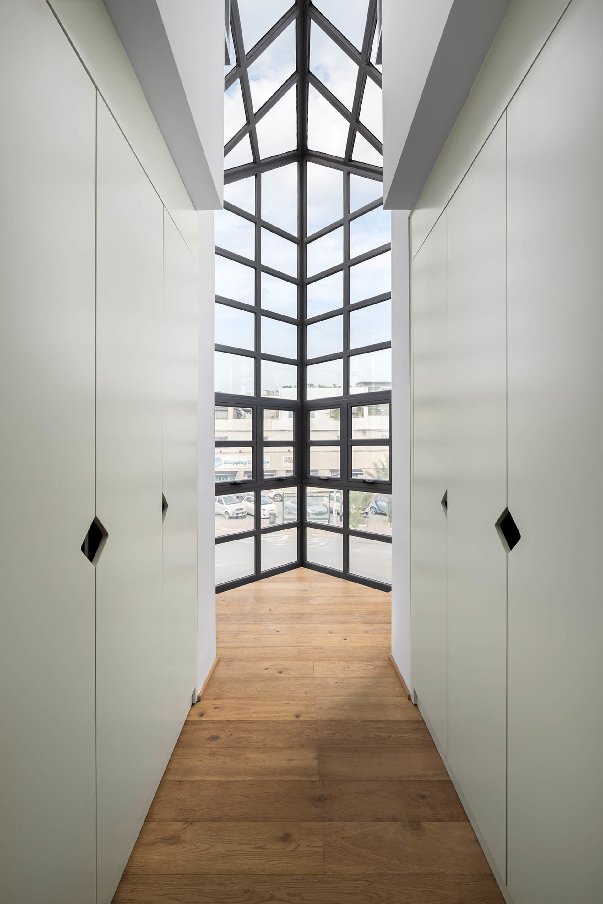 A modern, light-filled hallway with a glass ceiling and wooden floor.