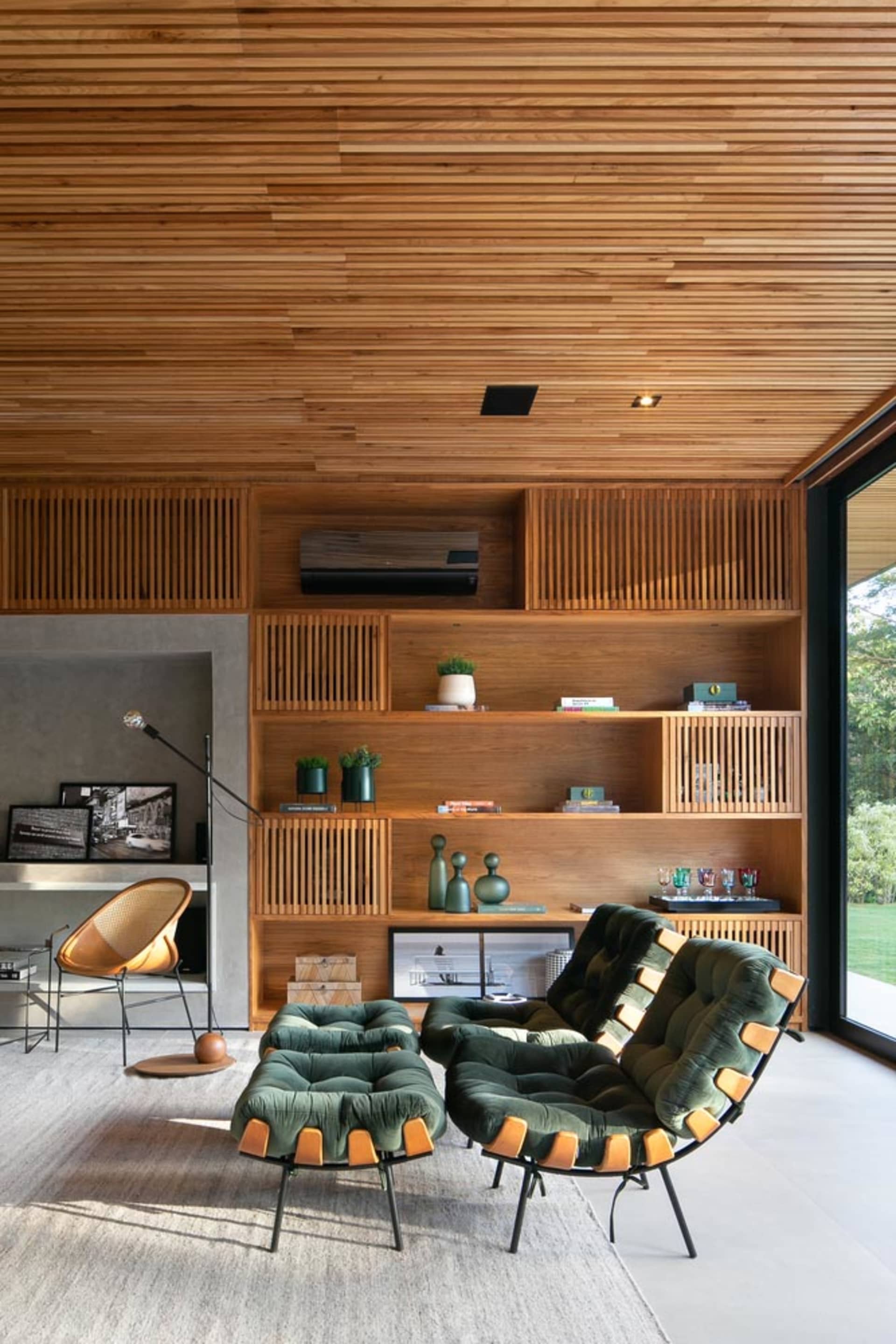 A modern living room with wooden shelves, green upholstered chairs, and a concrete fireplace.
