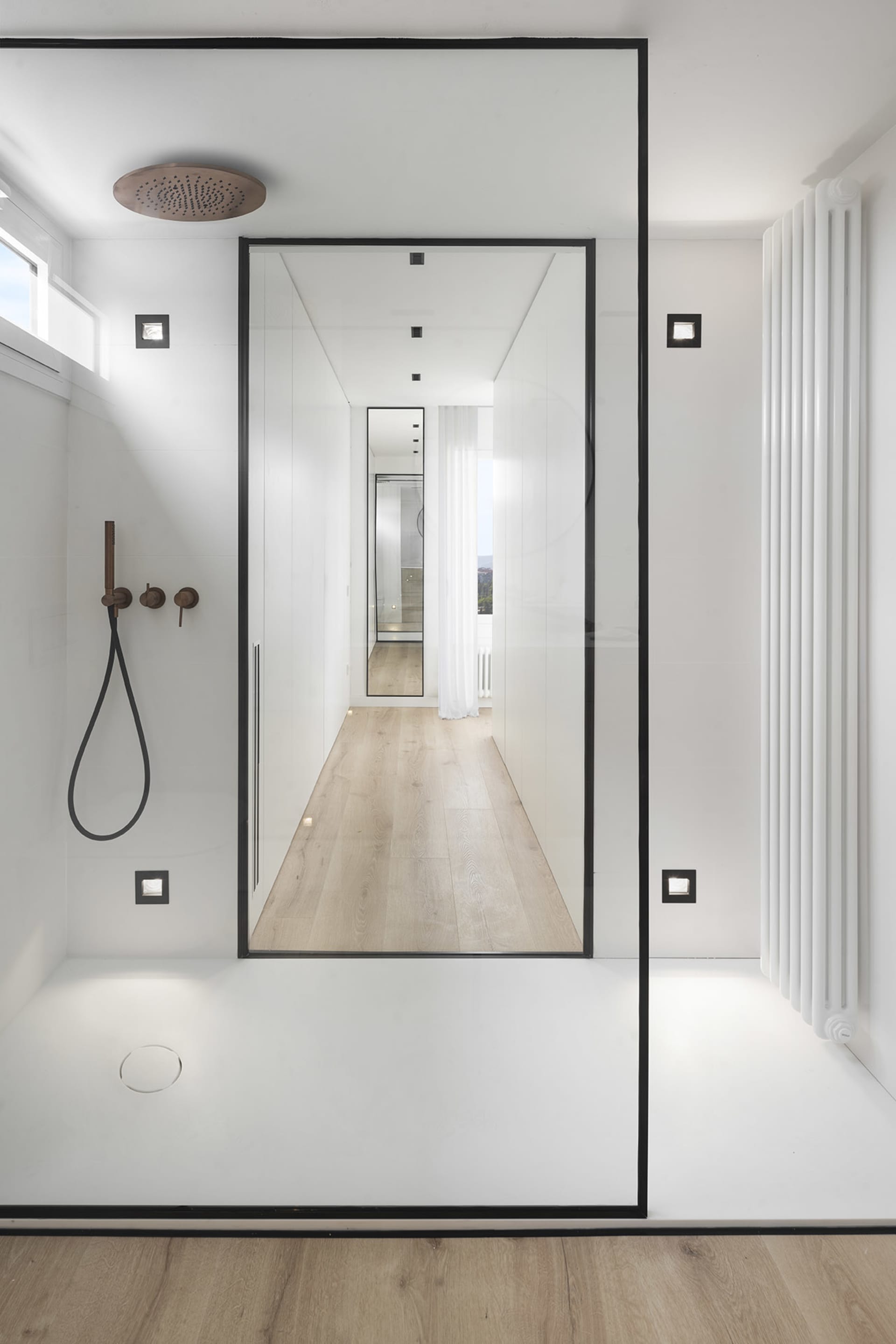 A minimalist bathroom with white walls and a glass shower enclosure.