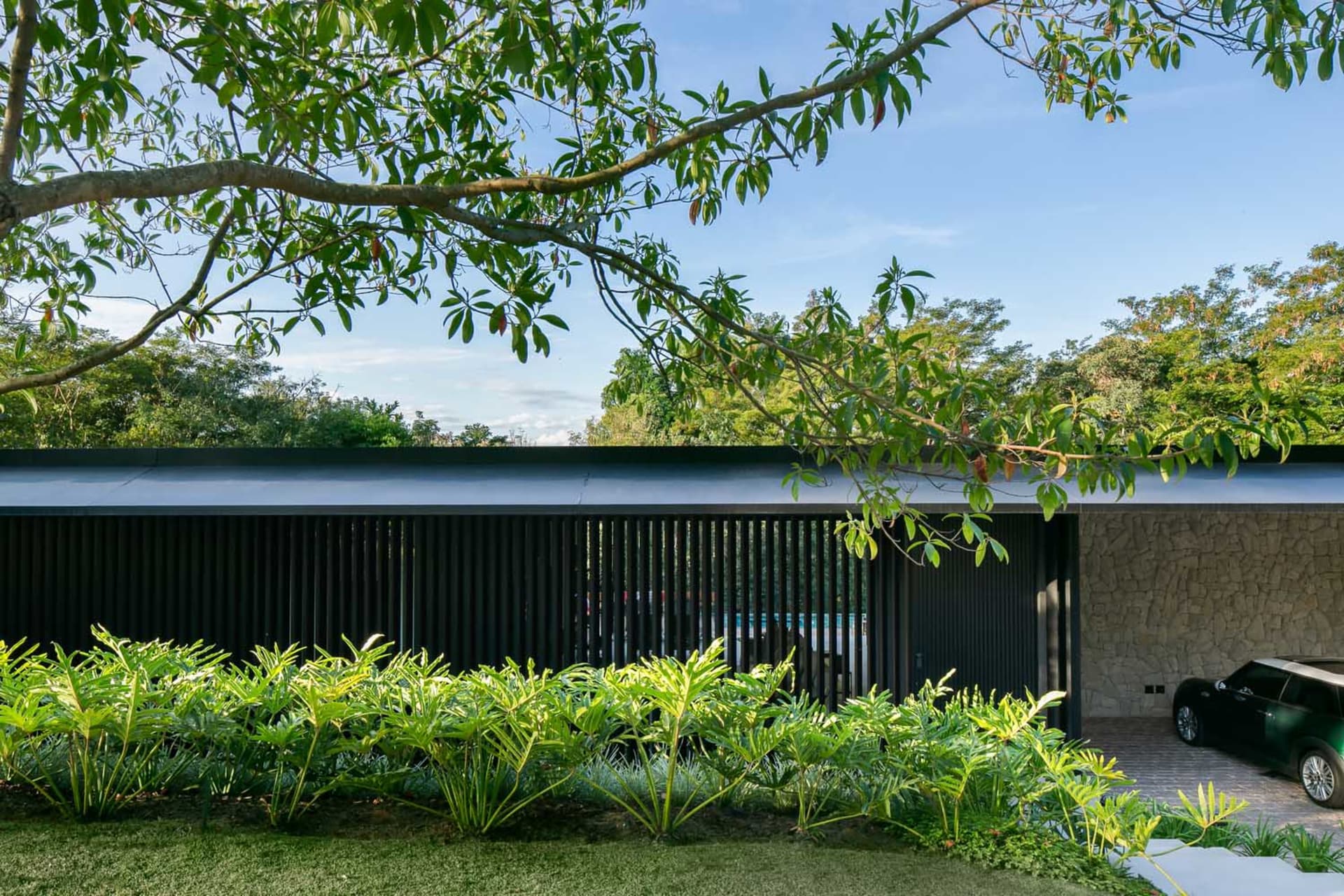 A modern house with metal panels and stone walls, surrounded by lush greenery.