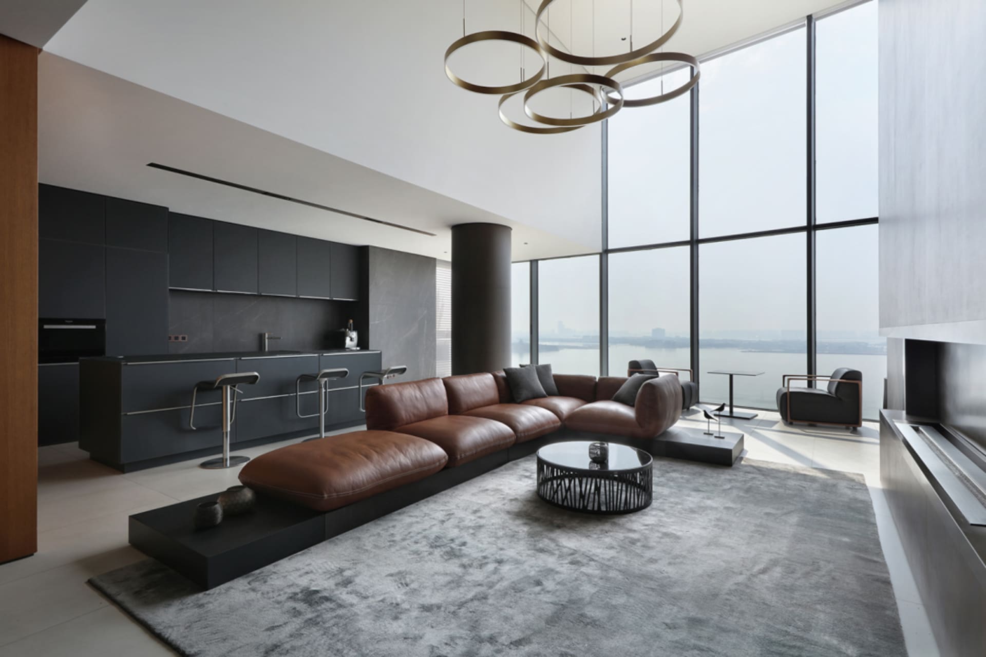 Modern living room with a leather sofa, coffee table, and large windows overlooking a body of water.