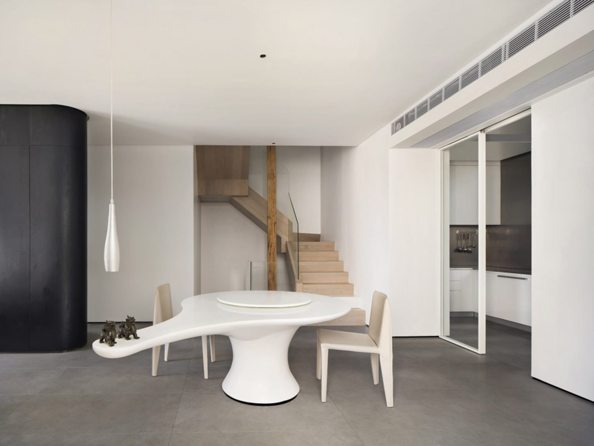 A modern, minimalist dining room featuring a sleek, white, organic-shaped table with a circular centerpiece, surrounded by th