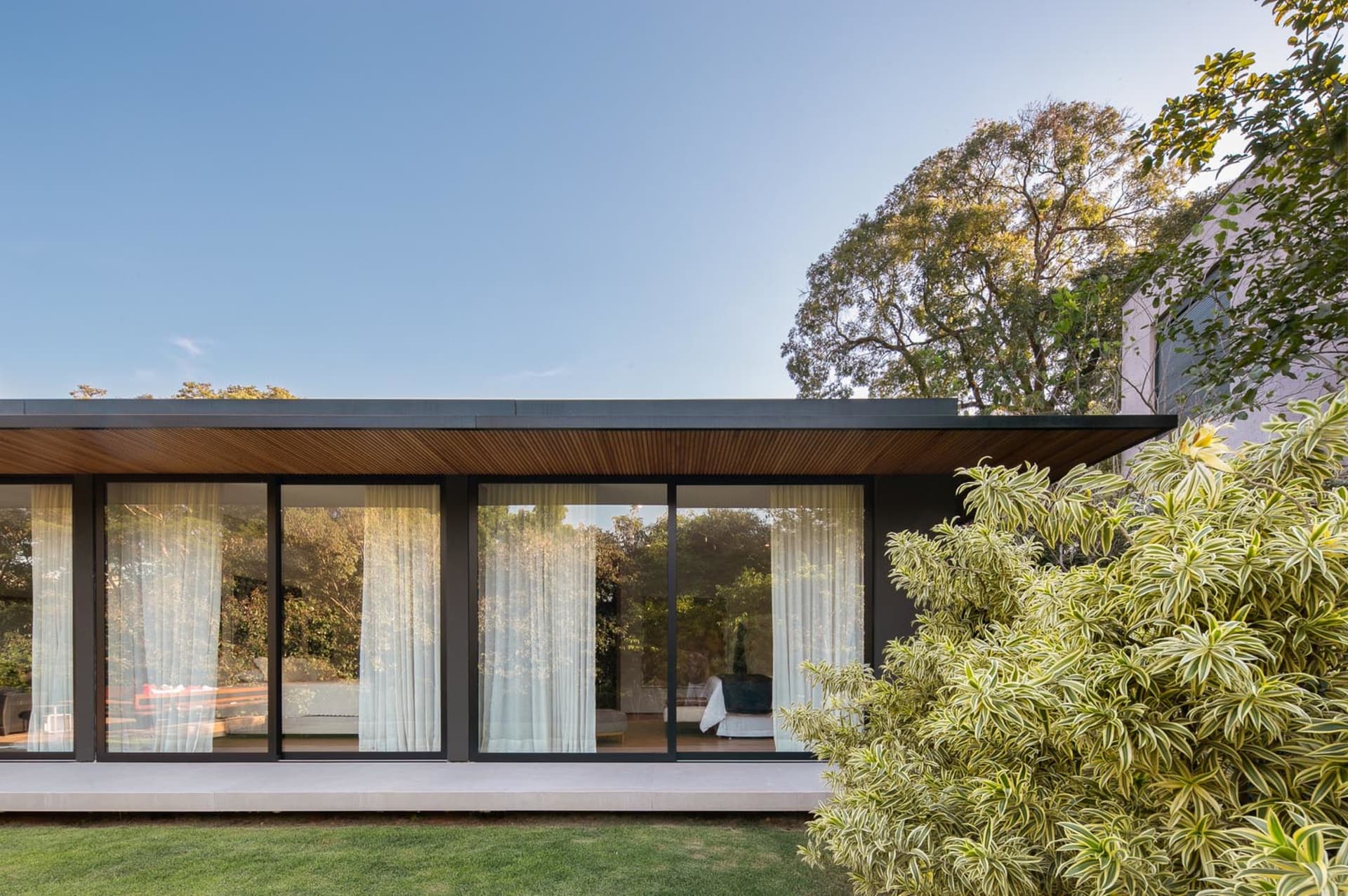 A modern residential exterior with large glass windows and a wooden roof.