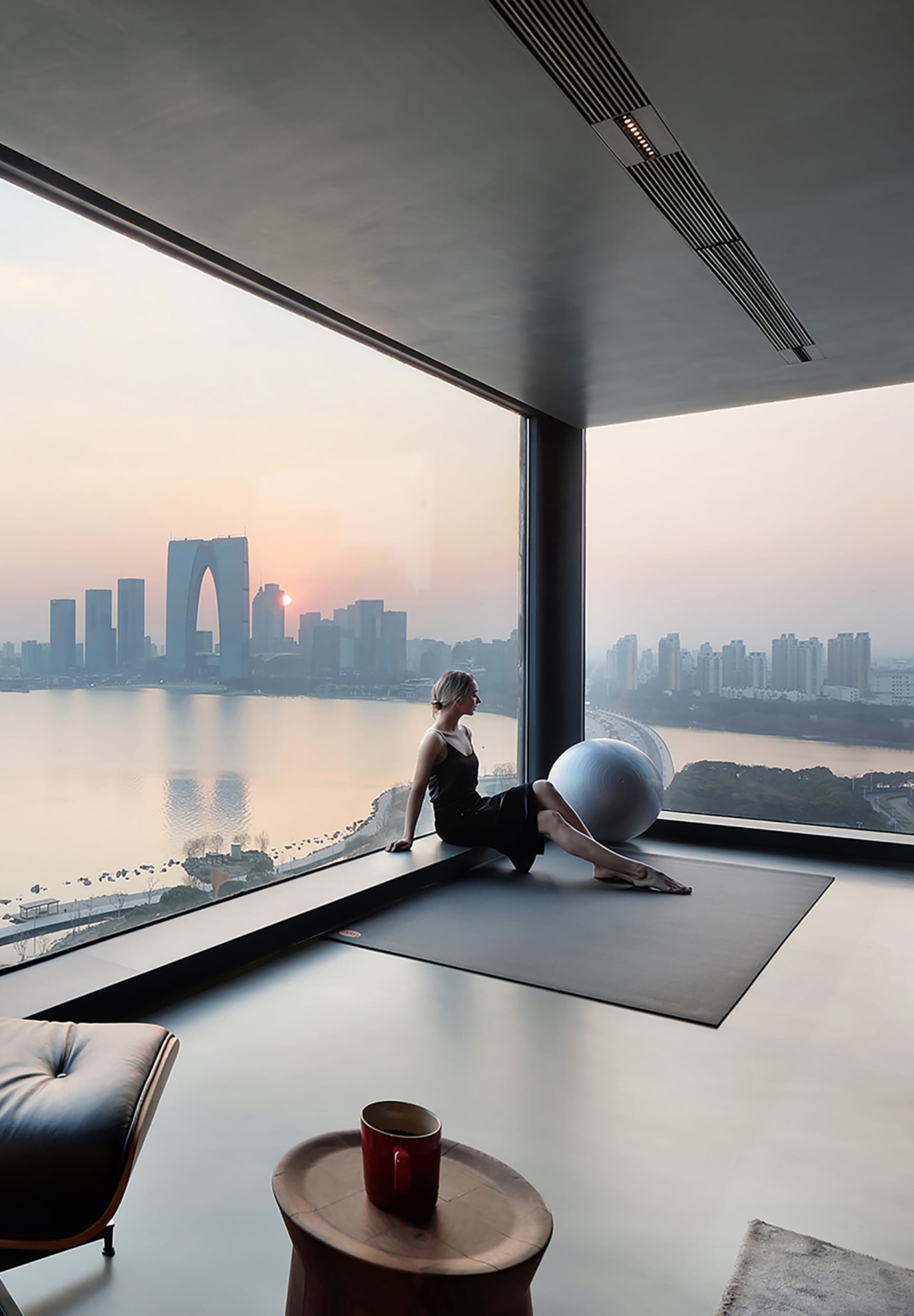 Person exercising on a workout mat in a modern room with concrete flooring, overlooking a city skyline.