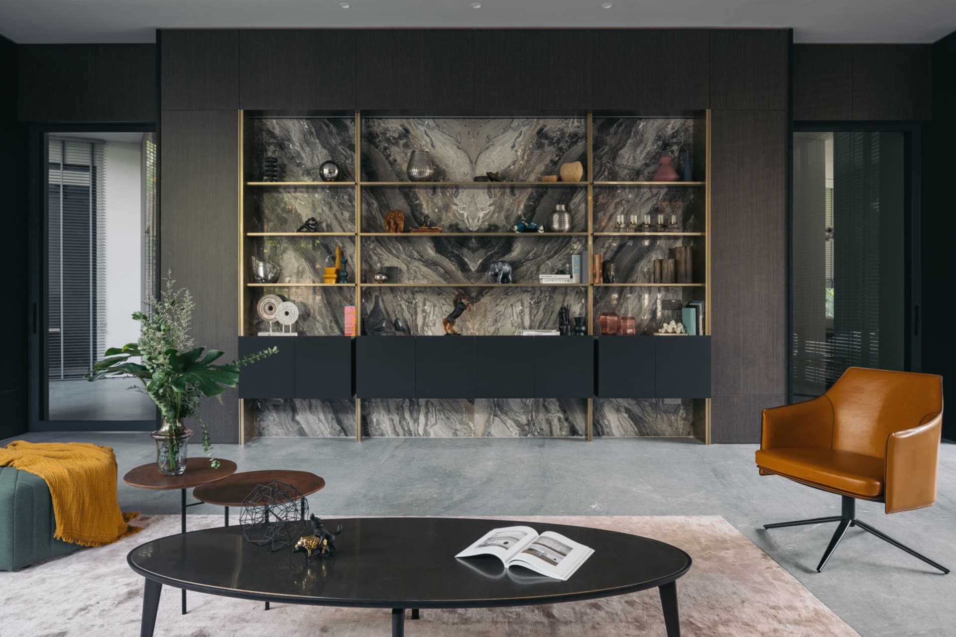 A modern living room featuring a marble wall with decorative objects and a mix of black furniture and a brown leather armchai