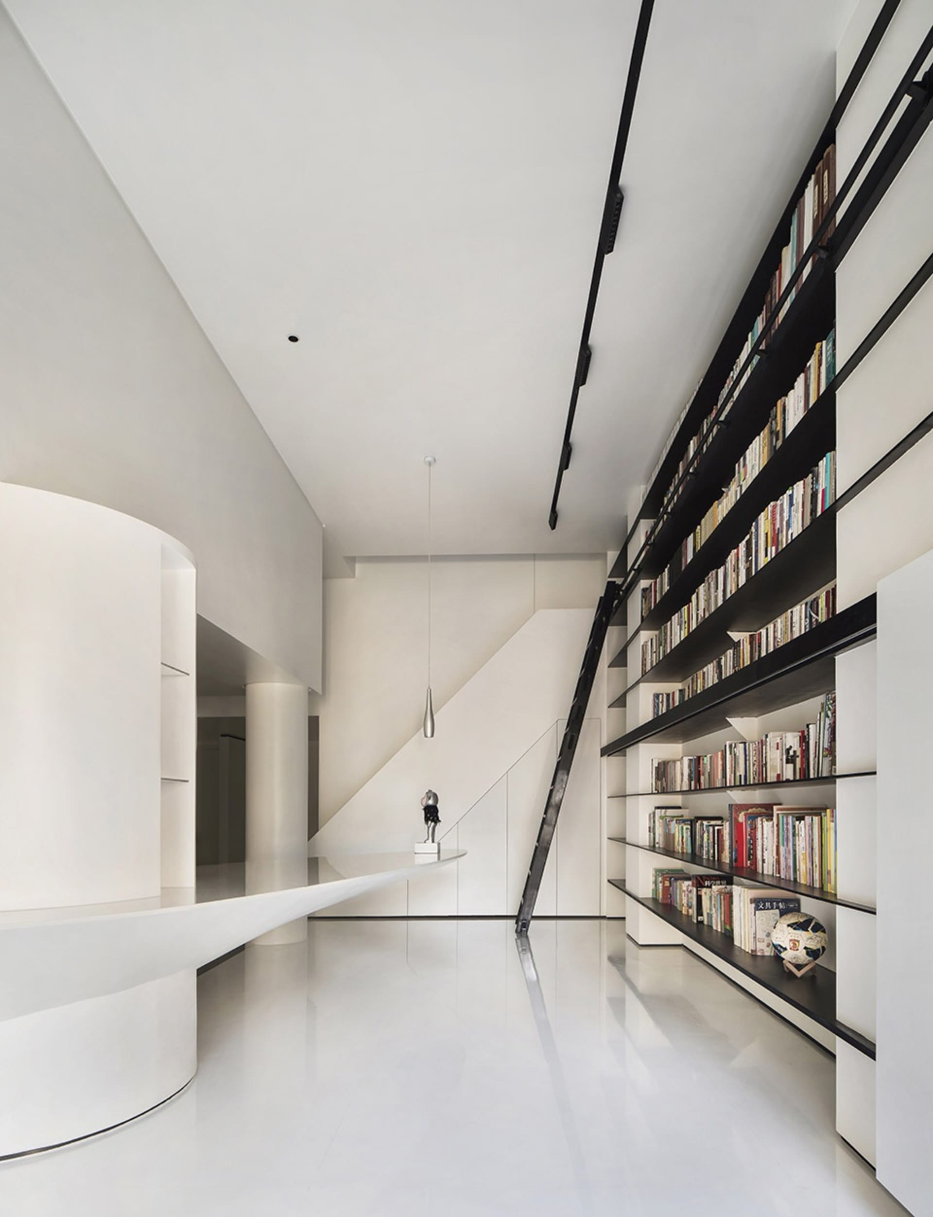 A modern library with a stairway leading to upper levels, featuring black metal shelves holding numerous books.
