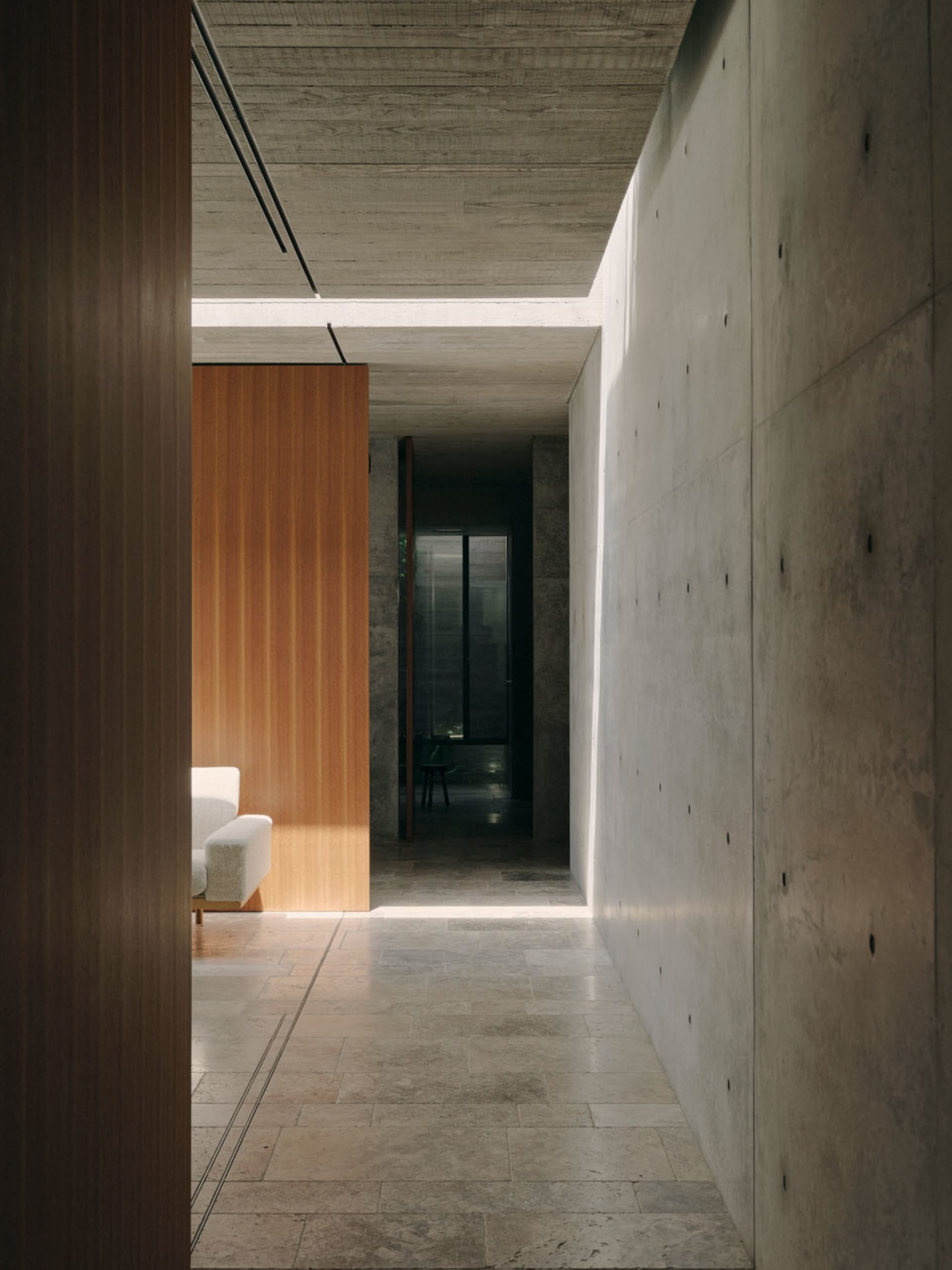 Minimalist design corridor featuring concrete walls and floor, with a wooden partition and a white sofa in the background.