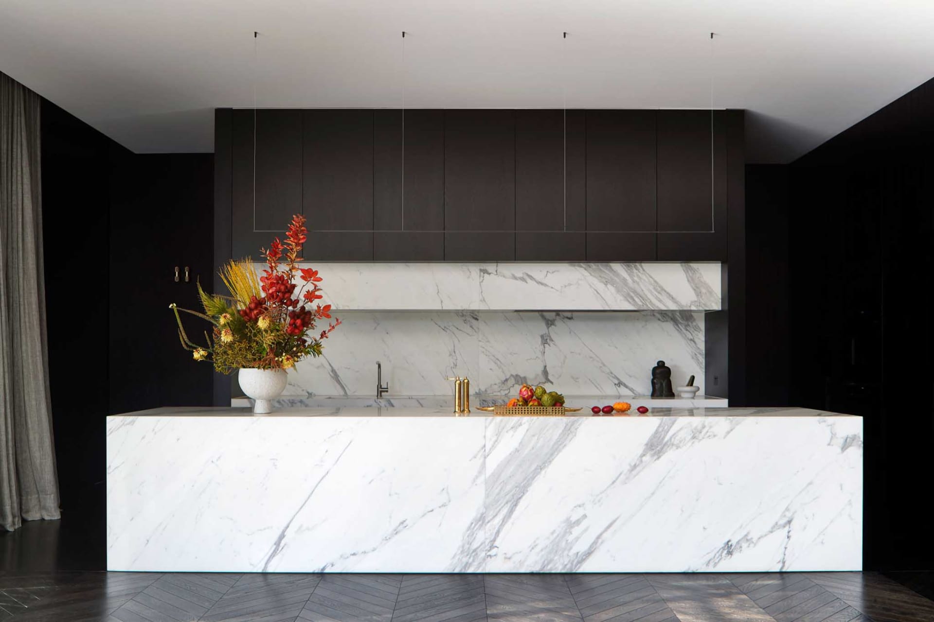 Modern minimalist residential kitchen featuring marble countertops and backsplash with a vase of autumn flowers and various f