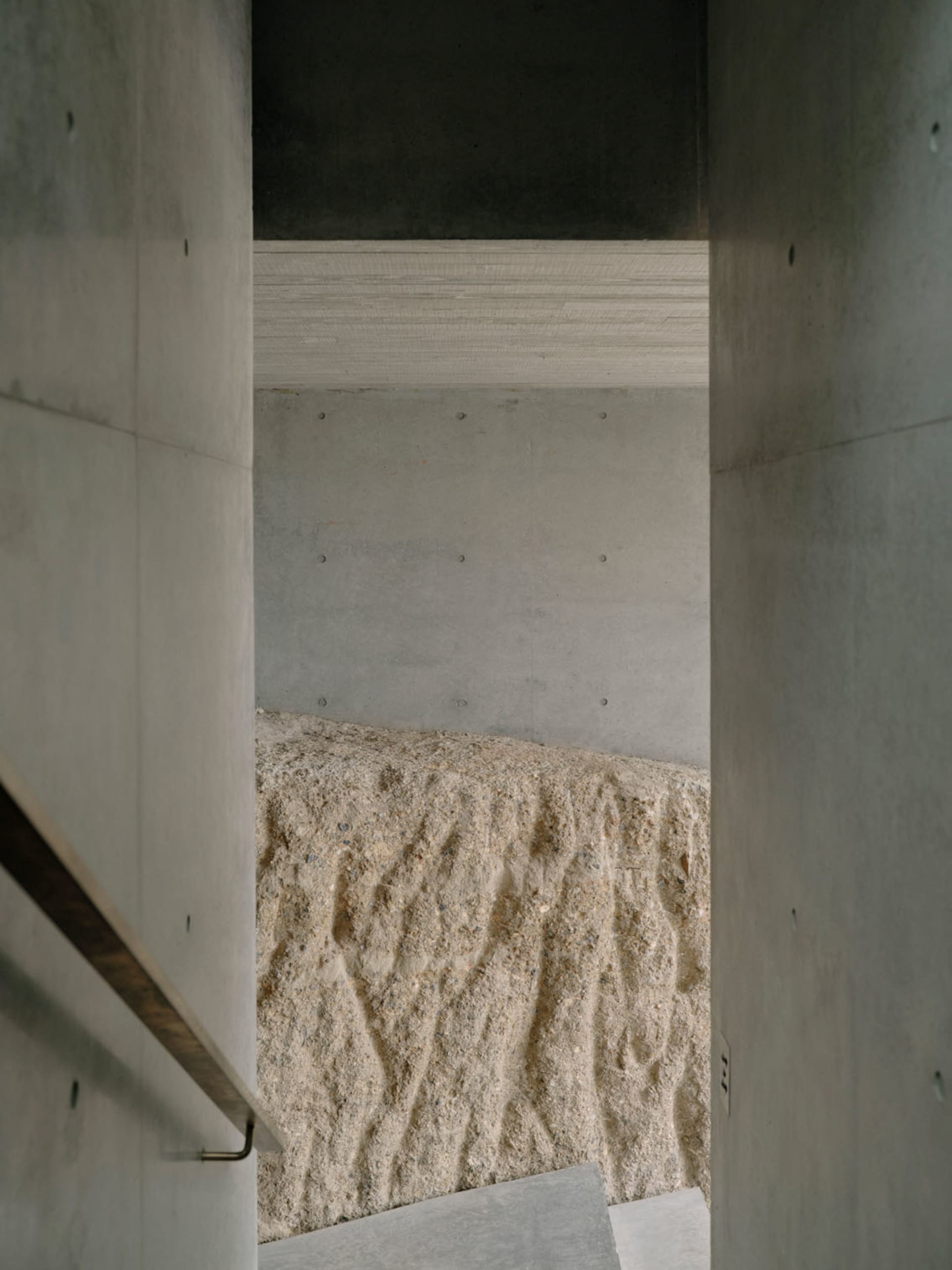 A modern interior space with concrete walls and sand floor, featuring minimalist design elements.