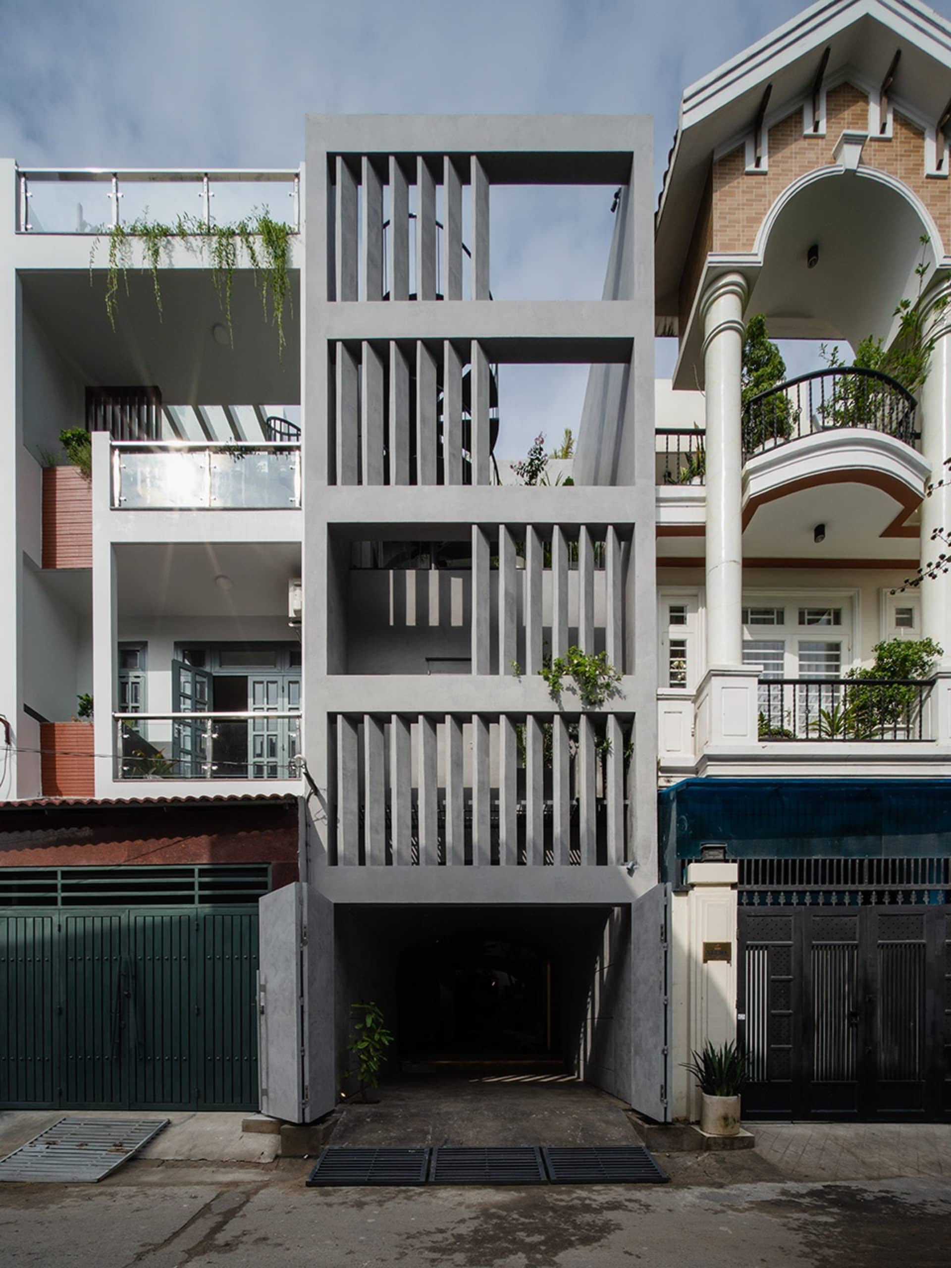 A modern residential entryway featuring a concrete structure with open, tiered levels and greenery on balconies.