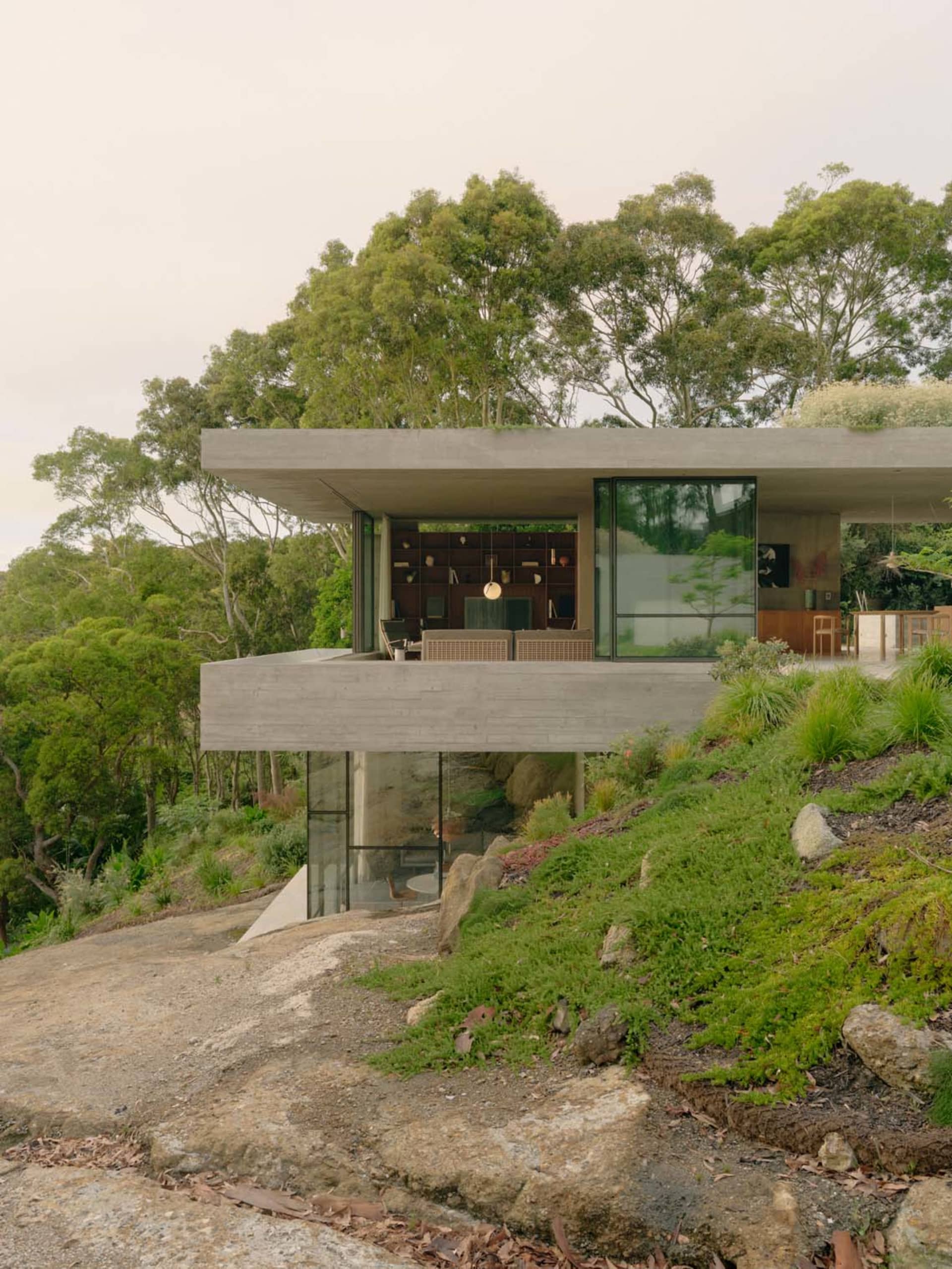 A modern minimalist cabin built into a hillside with concrete exterior and large windows.