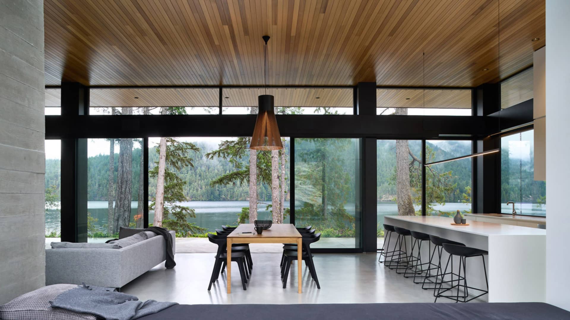 A modern residential space featuring a dining area with a wooden table and black chairs, a sofa, and a kitchen counter with s