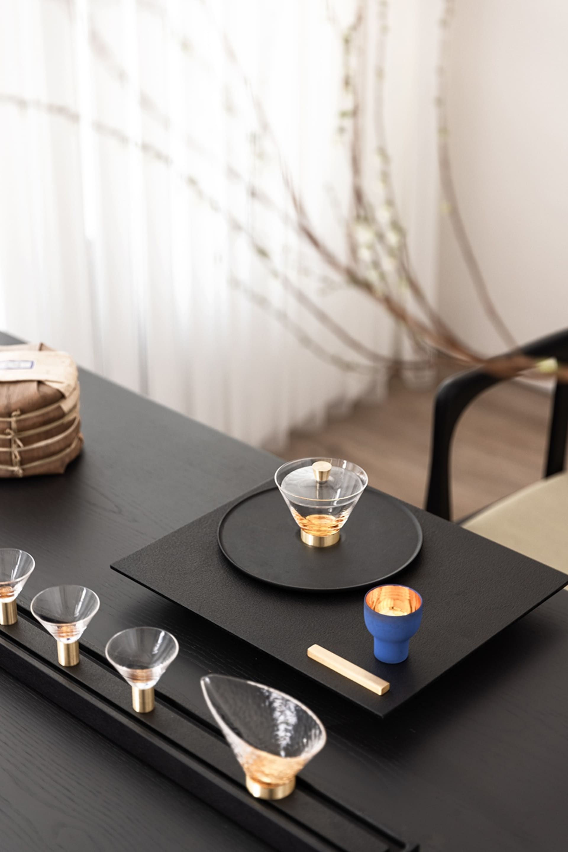 A meticulously arranged tea ceremony setup with glassware, ceramic items, and metal accents on a black table.