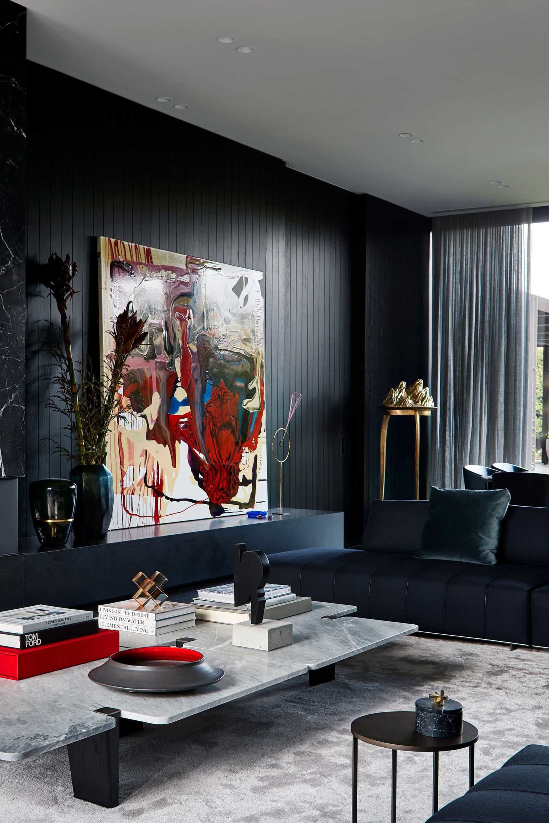 A modern living room featuring a concrete coffee table with leather seating, brass accents, and a large abstract painting.