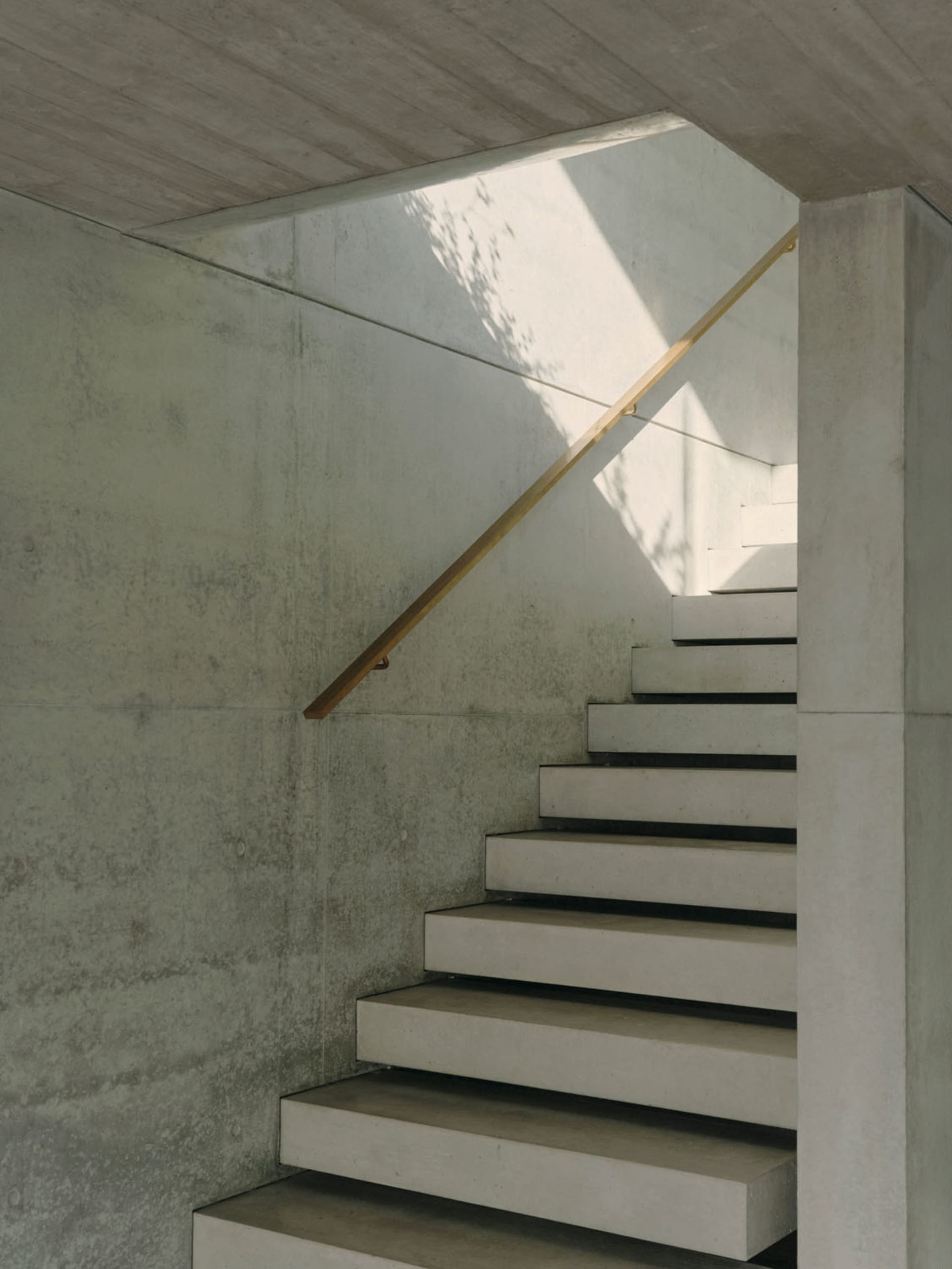 A minimalist staircase made of concrete with a wooden handrail, illuminated by natural light.