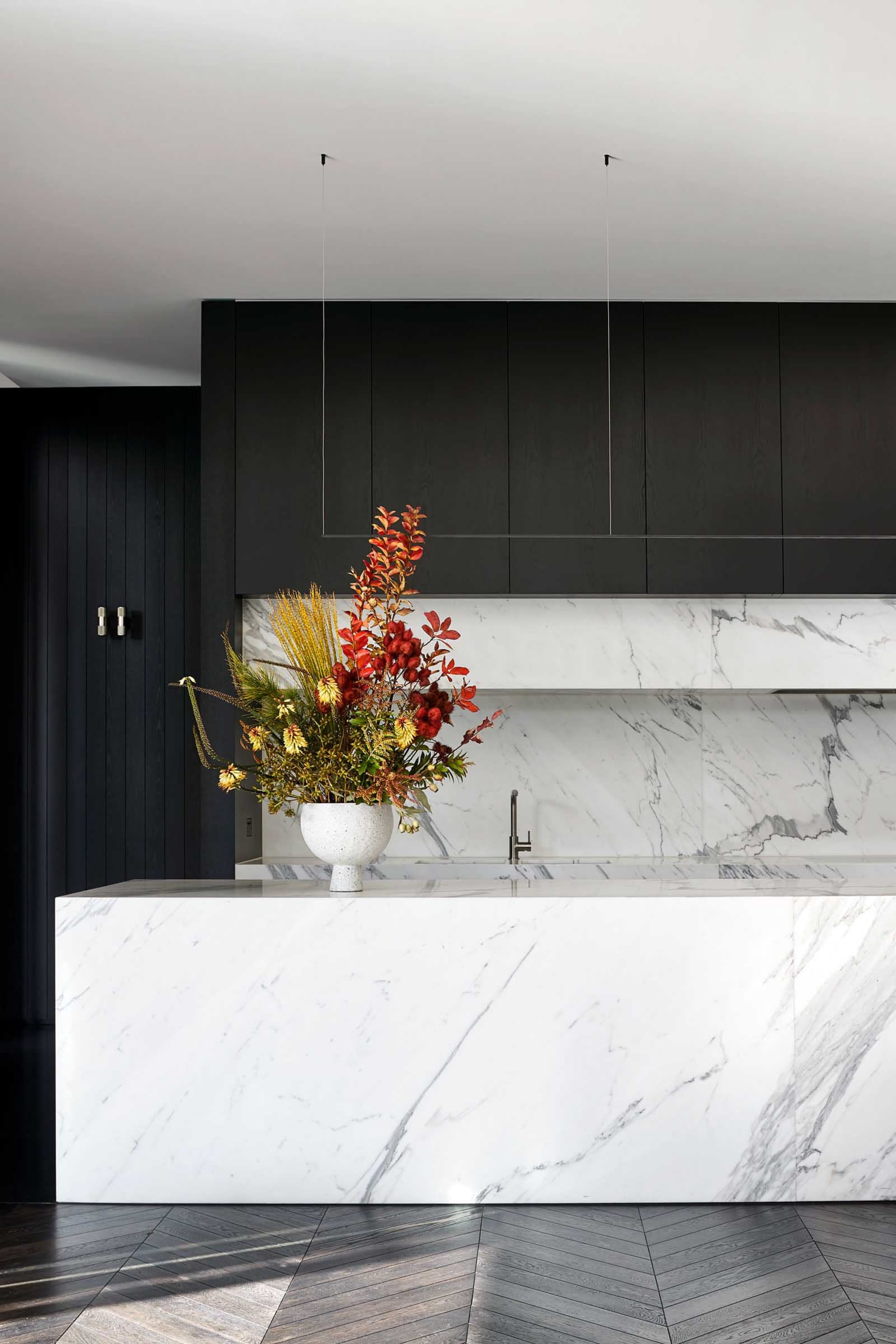 A modern kitchen with a large marble island featuring a vase of flowers and black cabinets.