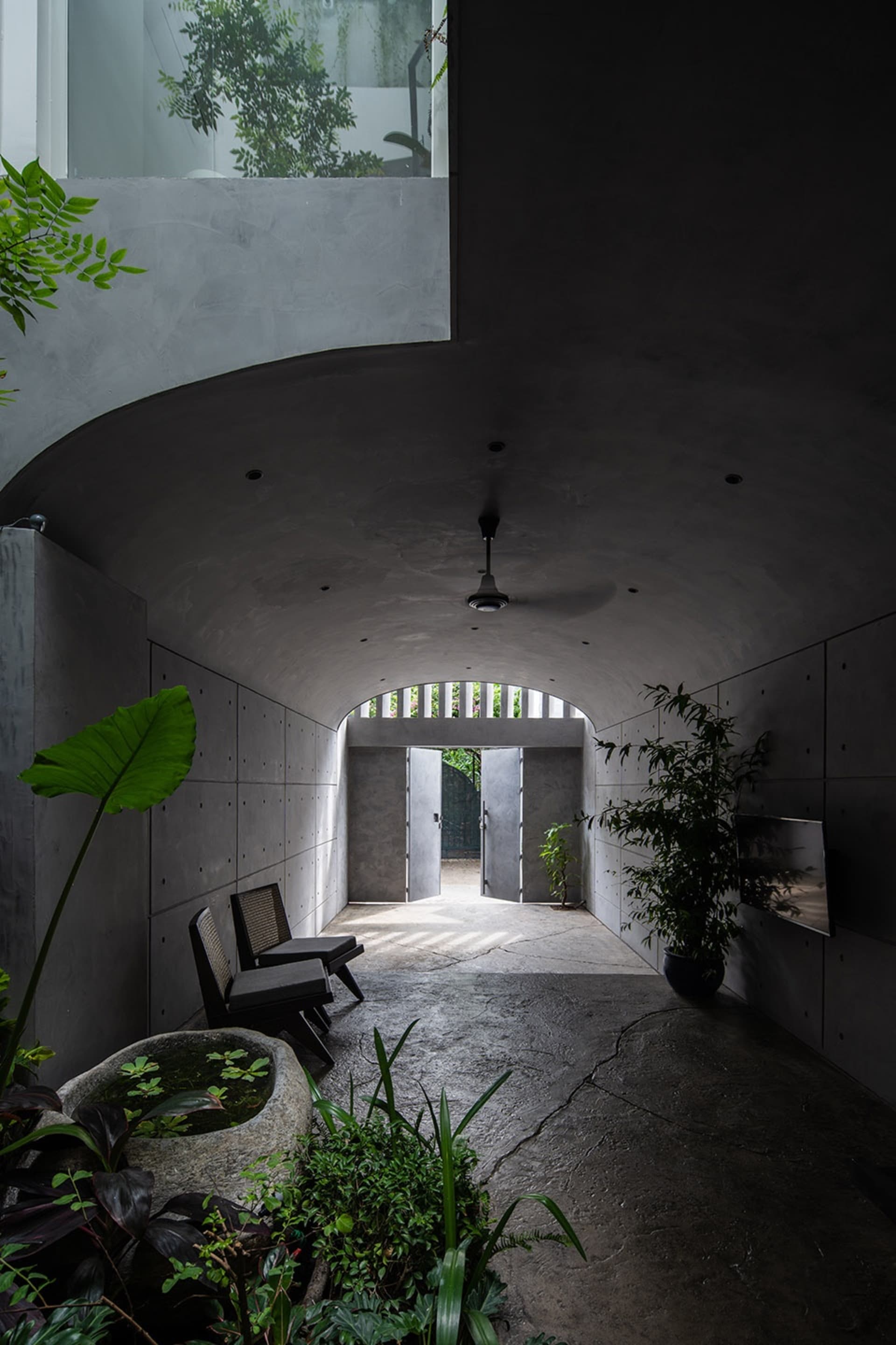 Modern indoor entrance with concrete walls and floor, plants, and natural light coming through an open door.