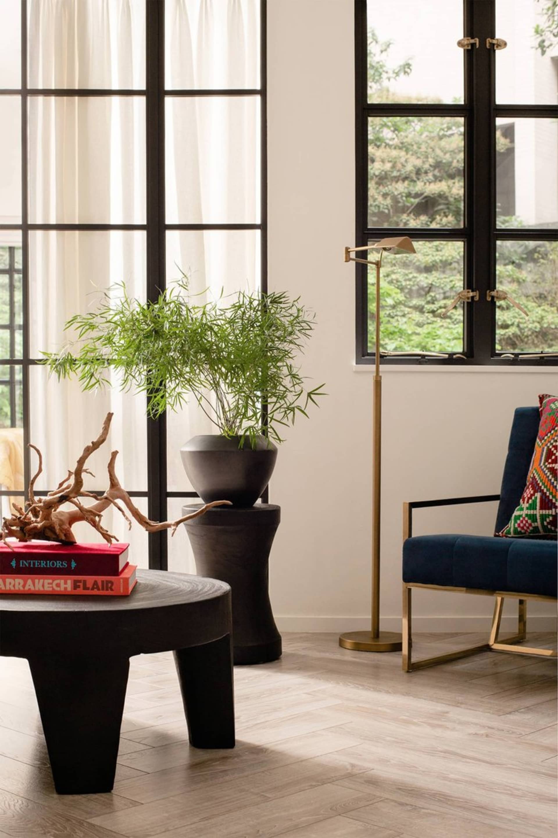 A minimalist living room featuring wood furnishings, a potted plant, and a floor lamp.