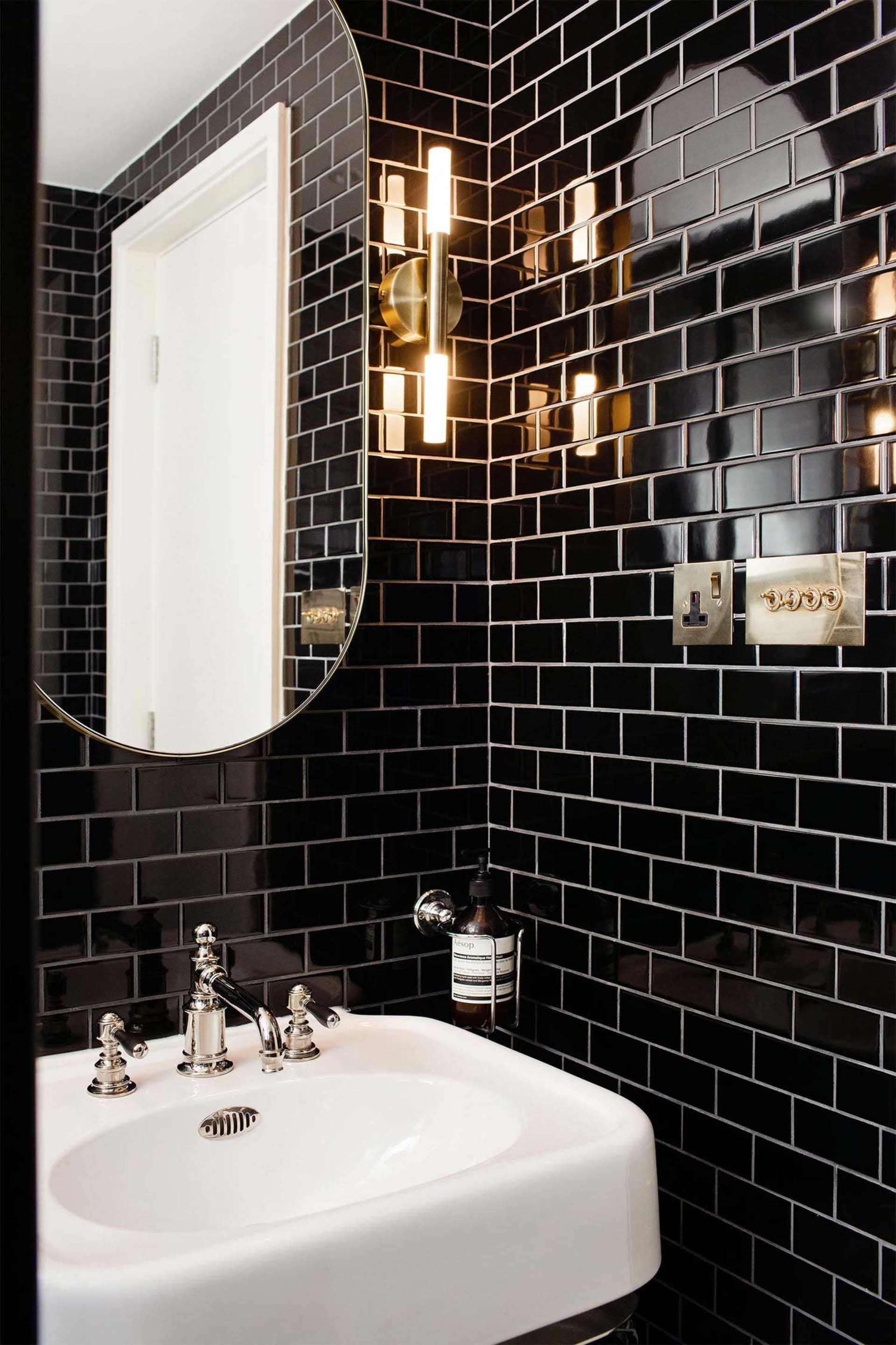 Modern black tiled bathroom with a white sink and gold accents