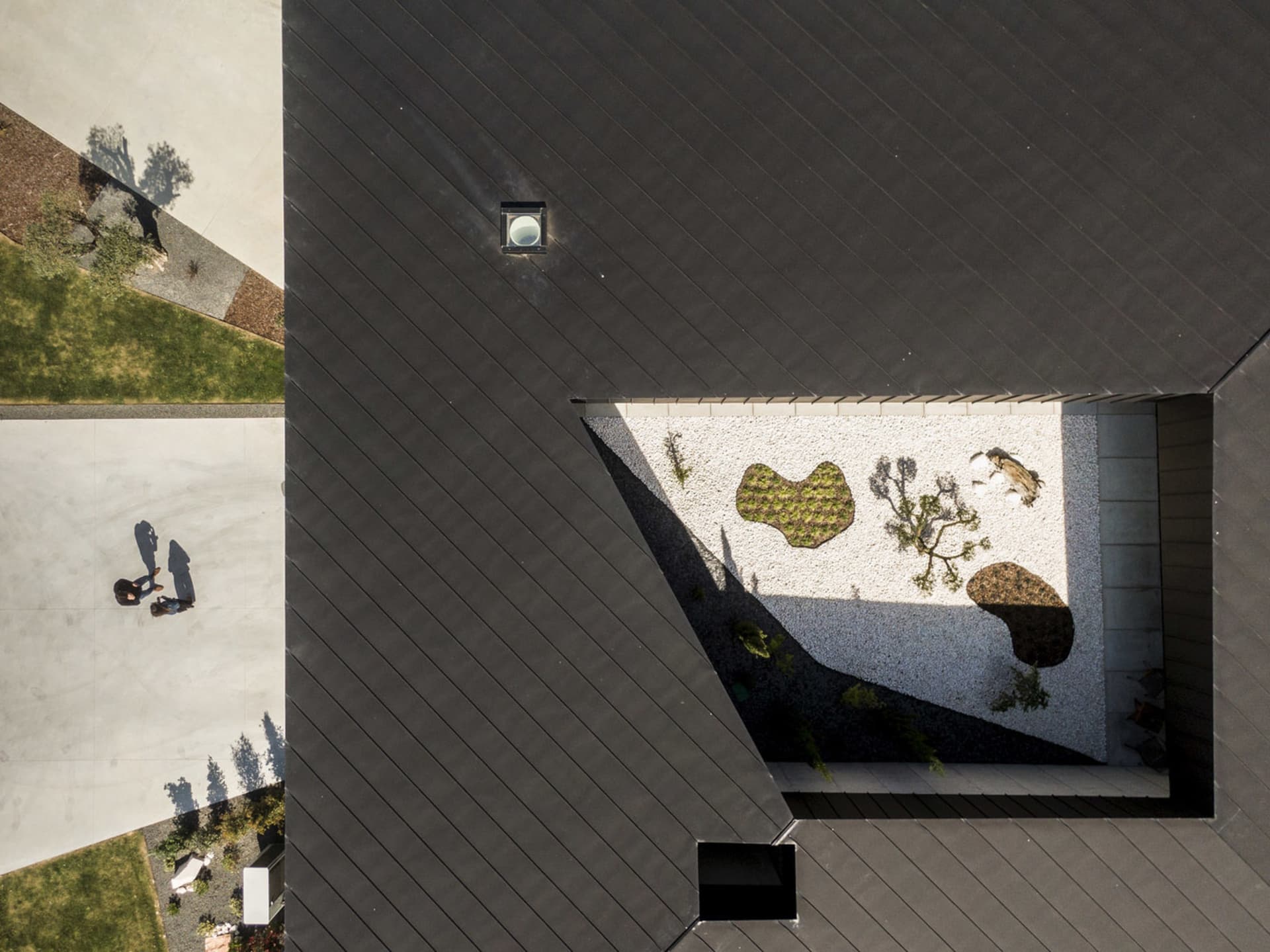 Top-down view of a modern rooftop garden featuring concrete and gravel surfaces with plants.