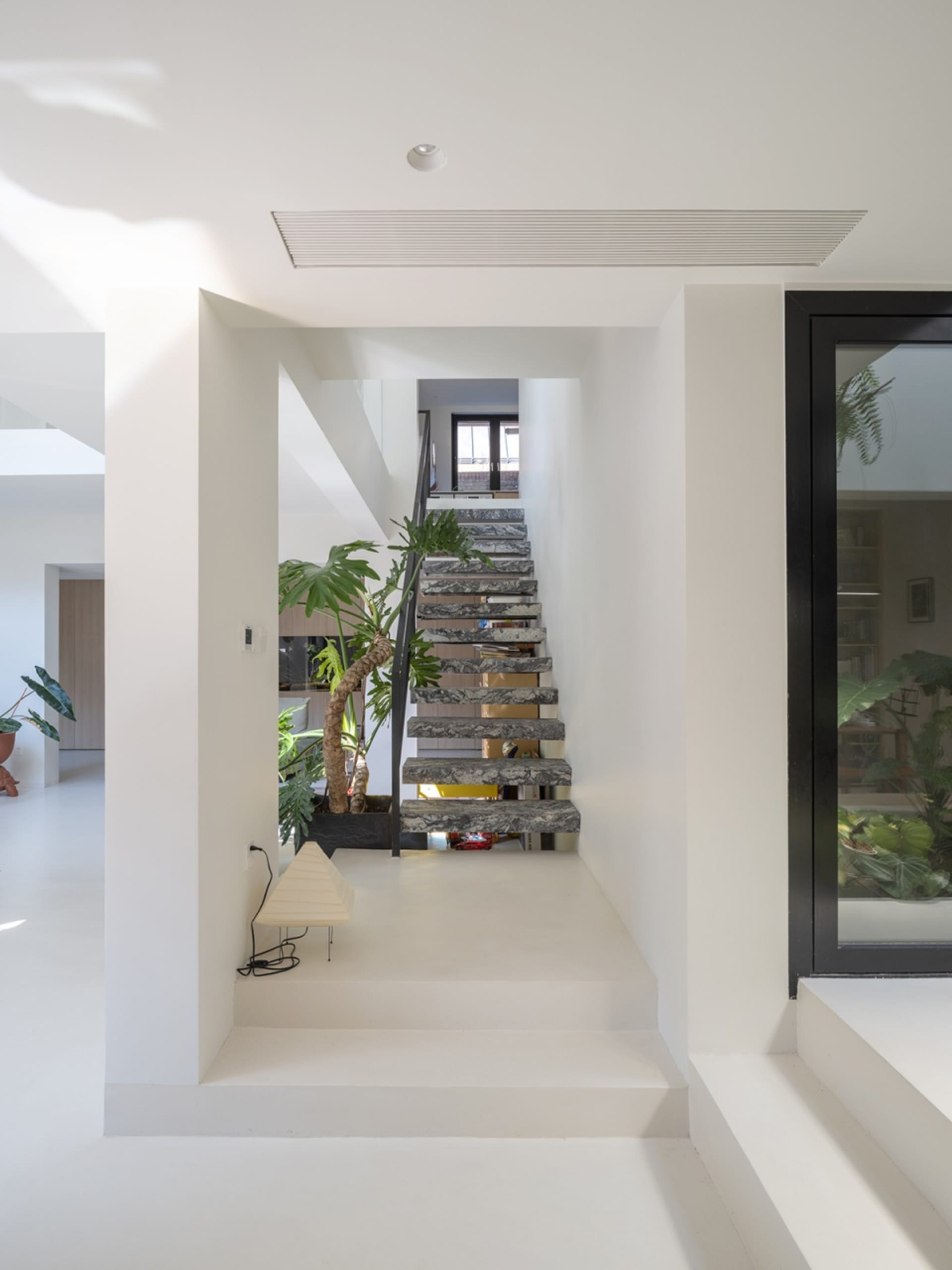 A minimalist staircase with marble steps and black railings, surrounded by white walls and plants.