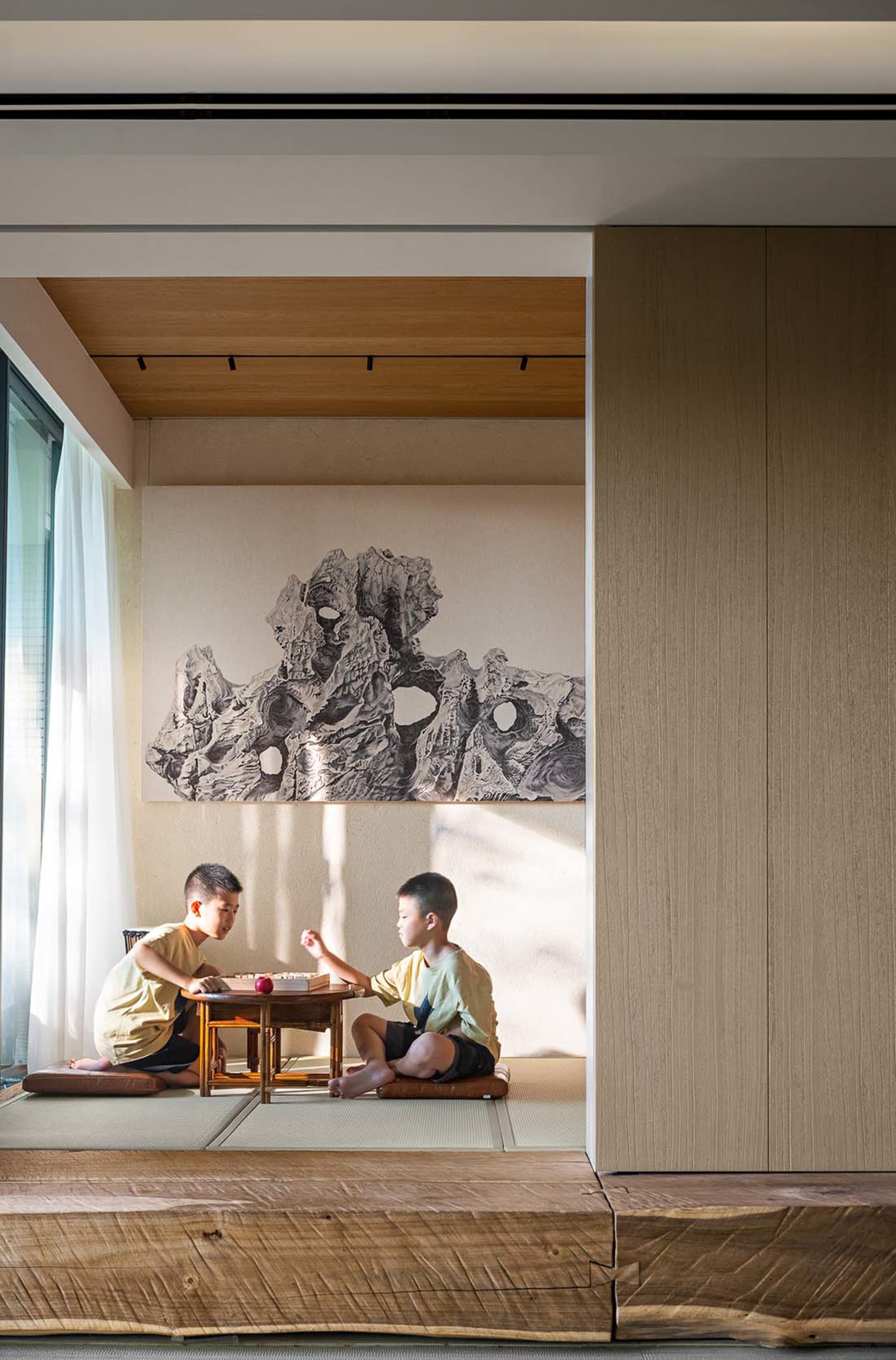 Two children playing a game on a wooden table in a modern living room with a natural stone mural on the wall.