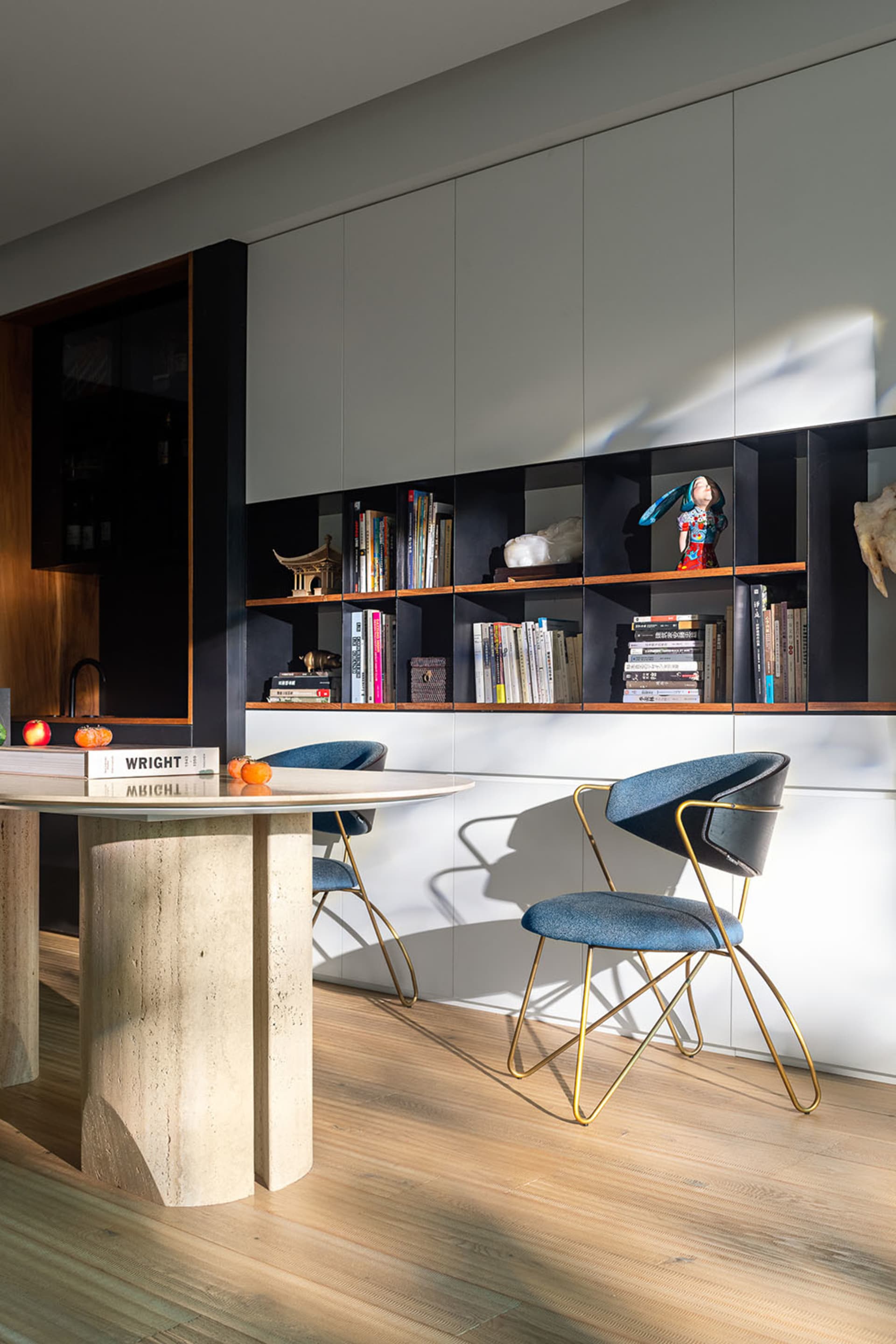 A modern living space featuring an open bookshelf with various books, decorative items, and a table with a stone base.