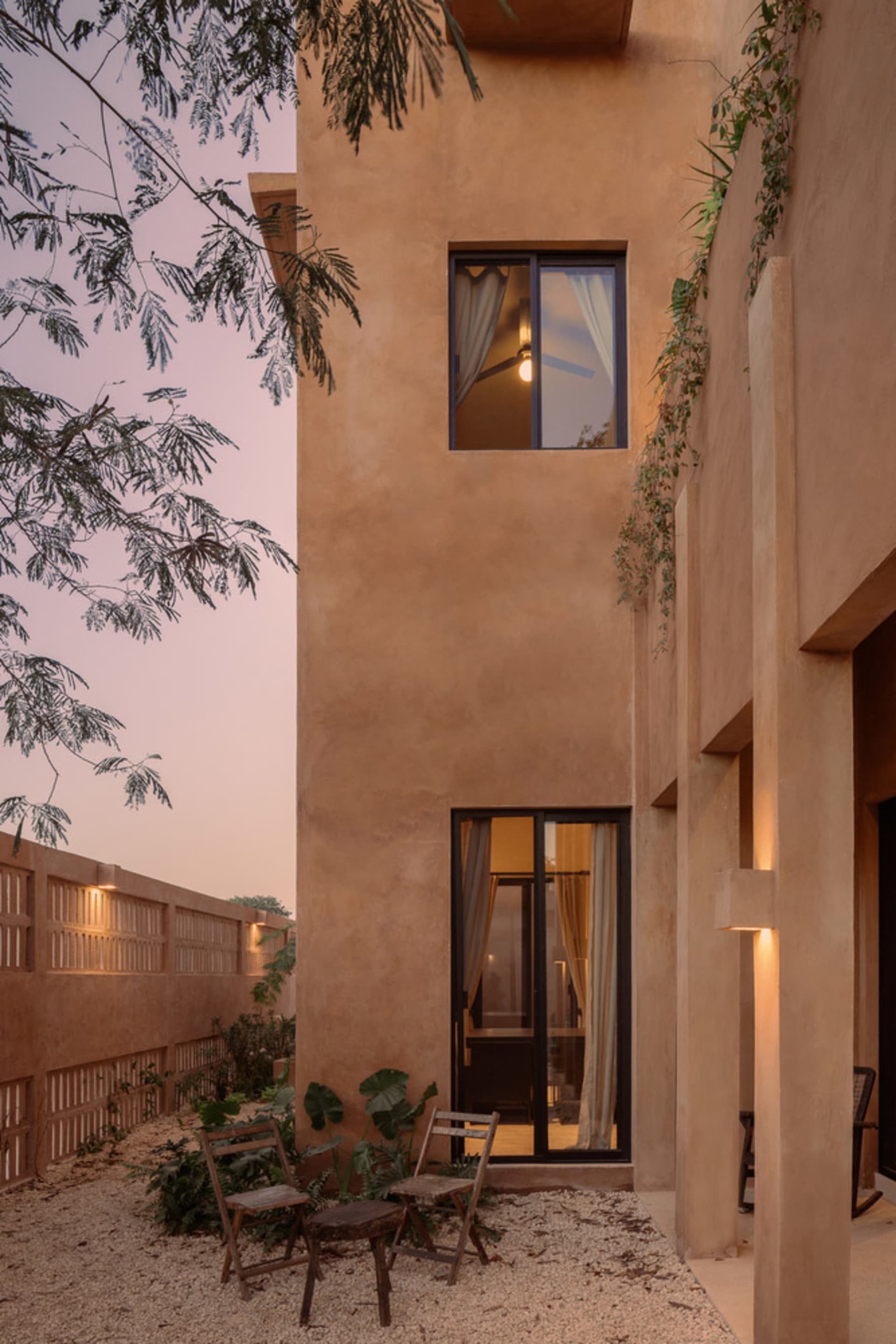 Modern residential exterior featuring clay-rendered concrete walls, a single-story structure with large glass window, and out