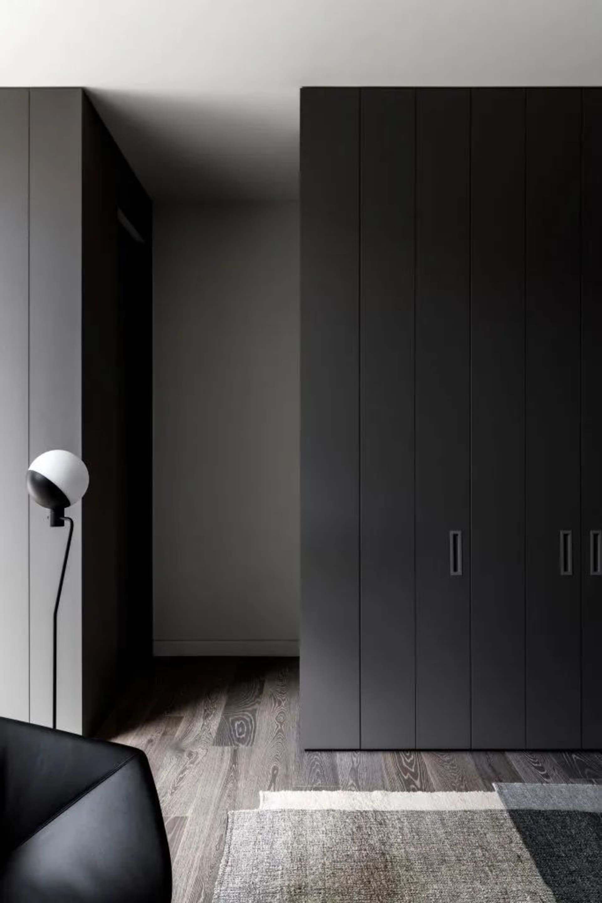 A modern minimalist living room featuring dark wood flooring, black metal and wood cabinets, and a white rug.