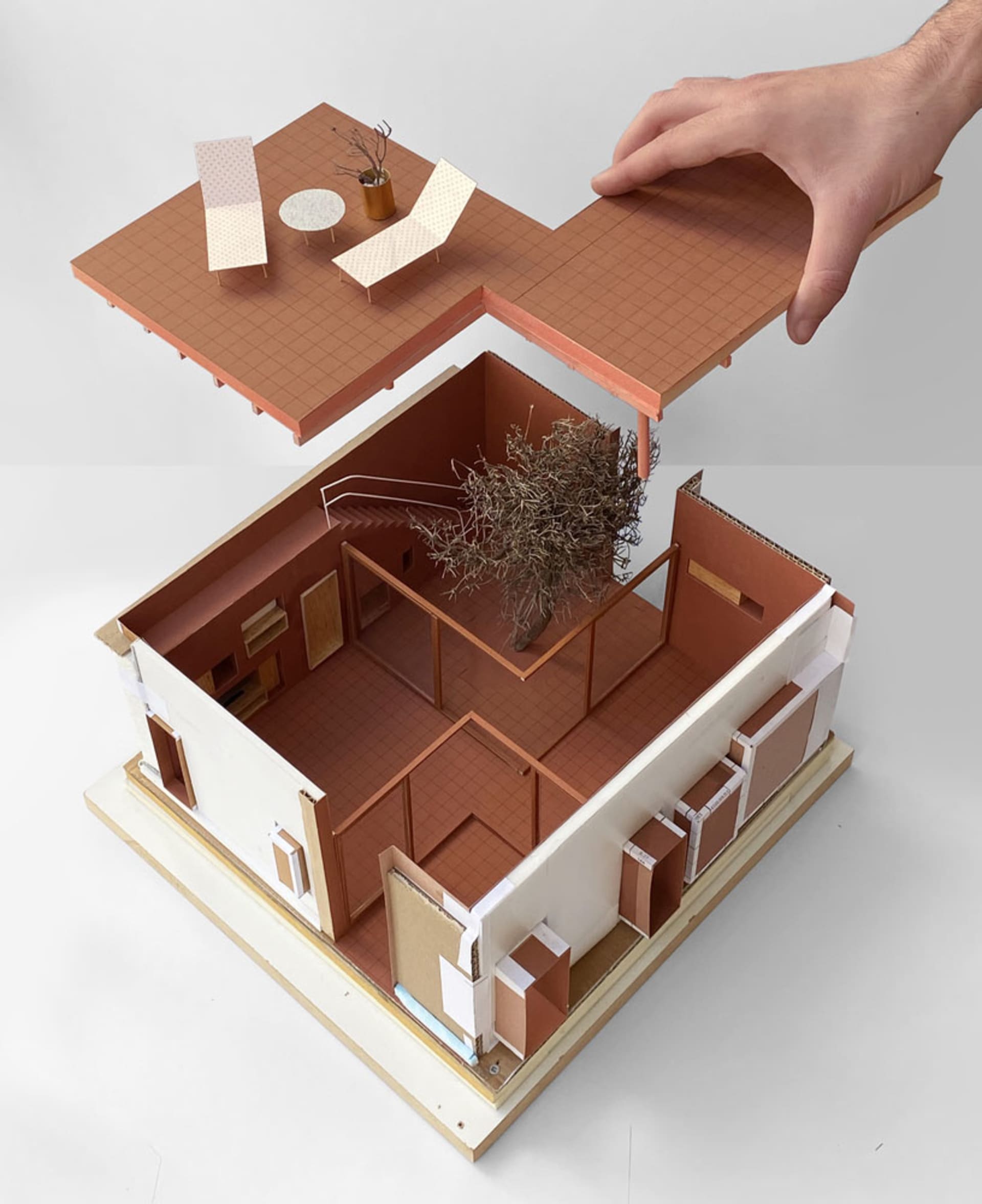 A model of a house made from paper and cardboard, with a tree inside and a hand lifting a section of the building.
