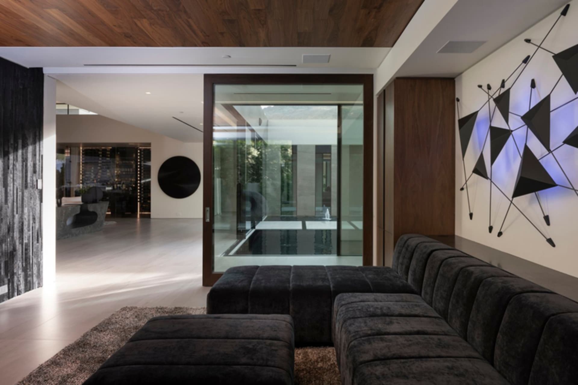 Contemporary living room featuring black leather furniture, metal elements, and a geometric wall art installation.