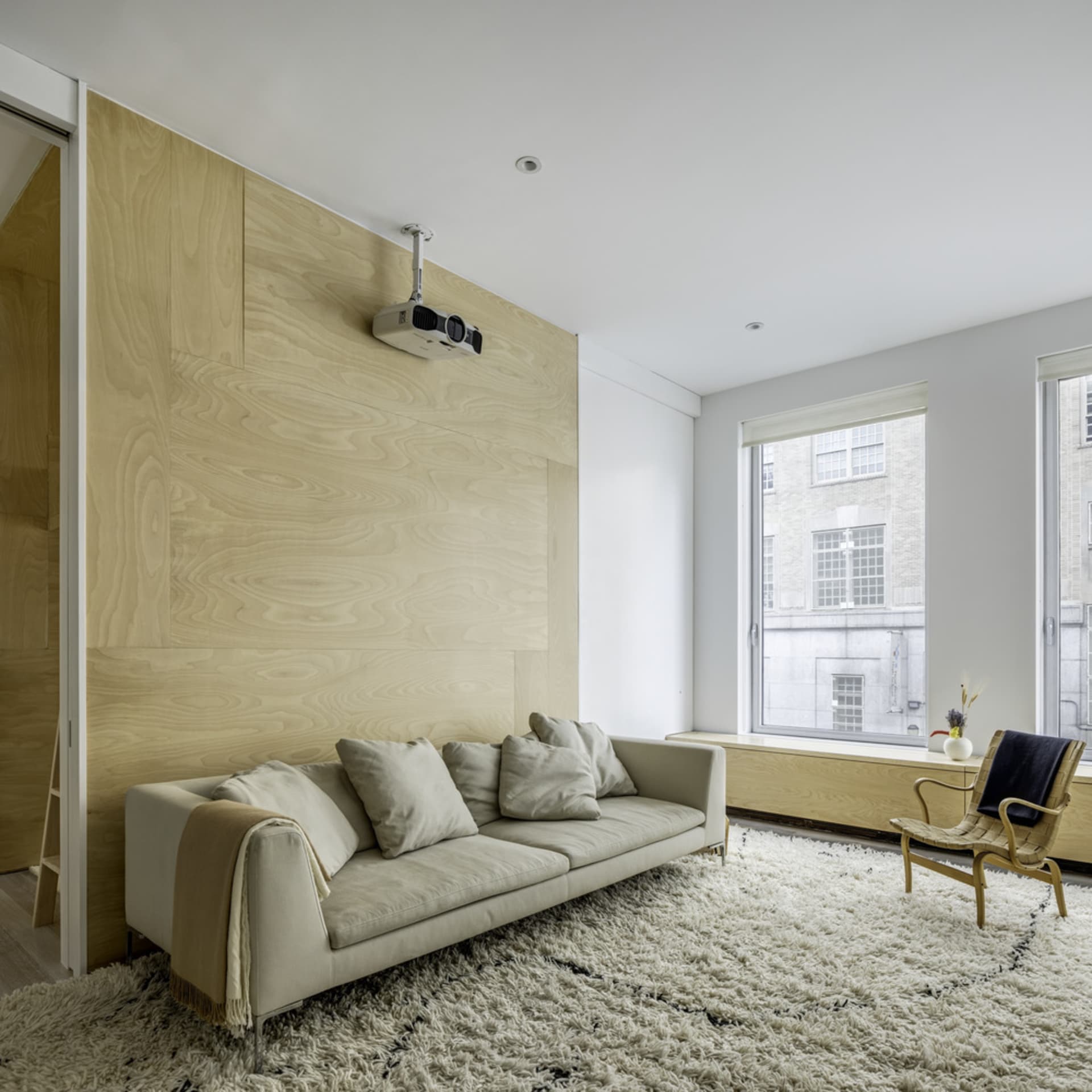 A modern minimalist living room with a wood accent wall, a white sofa, and a projector mounted on the ceiling.
