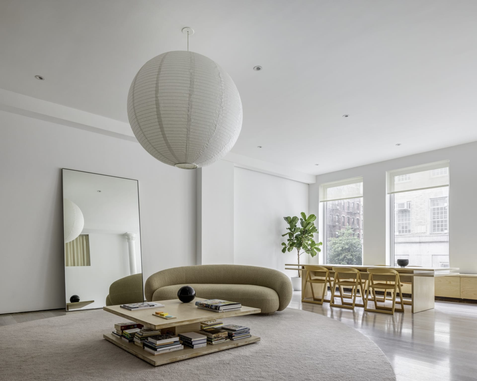 A modern, minimalist living room with a neutral color palette, featuring a curved sofa, wooden coffee table, and large floor 