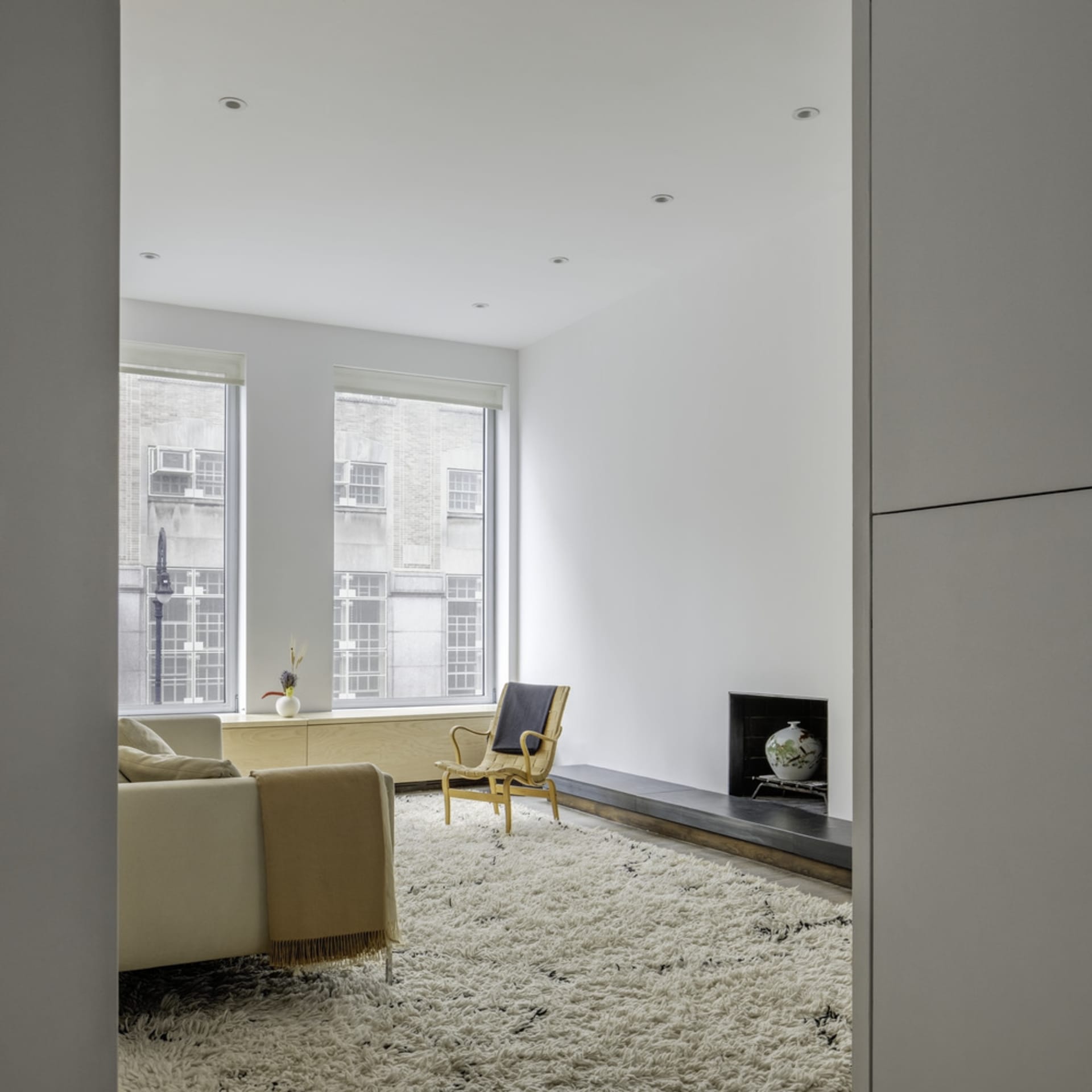 A minimalist living room with a white sofa, a yellow and wooden armchair, and a white fluffy rug.