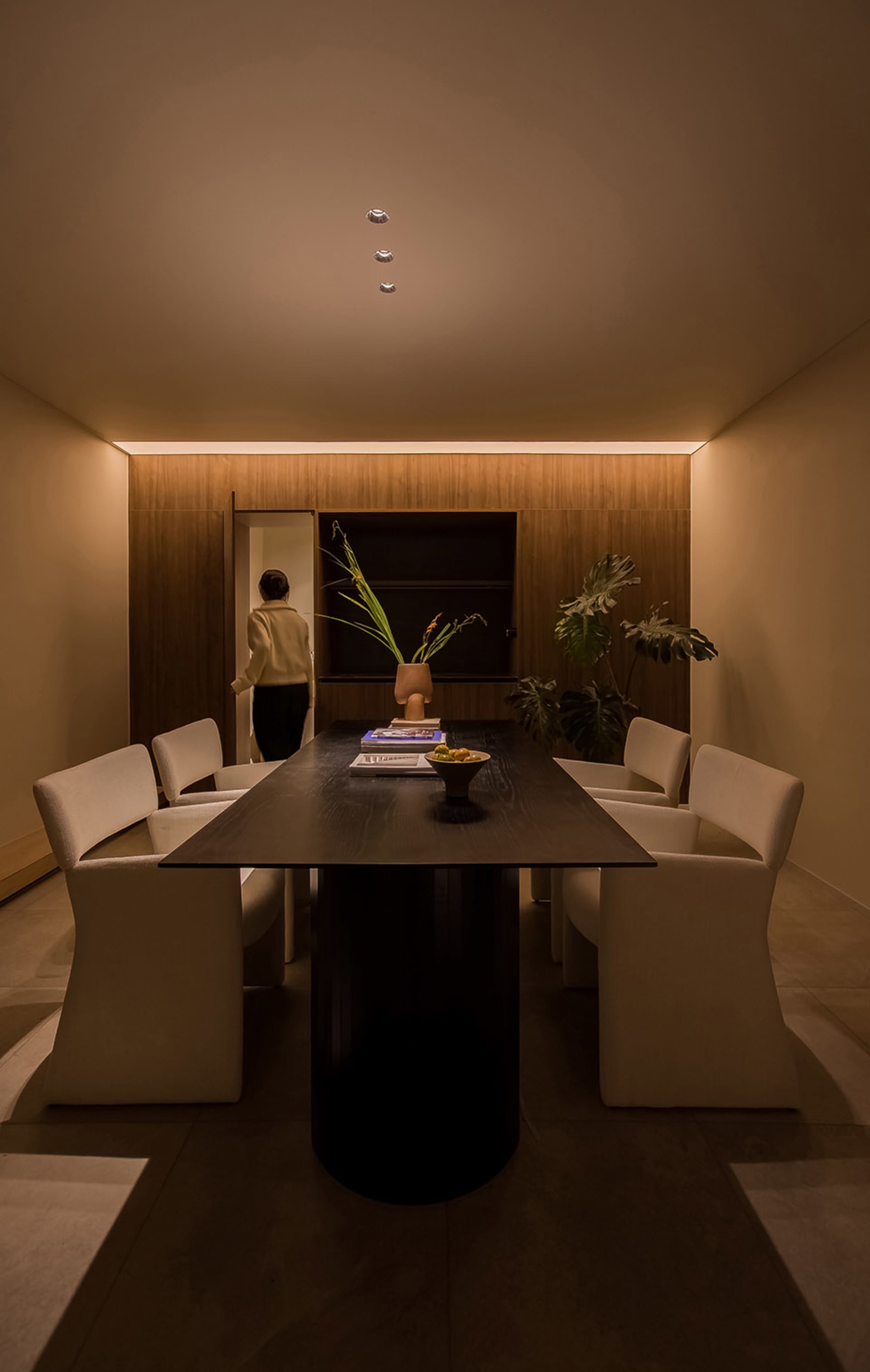 A modern interior space featuring a wooden table with white chairs, a vase of flowers, and a book.