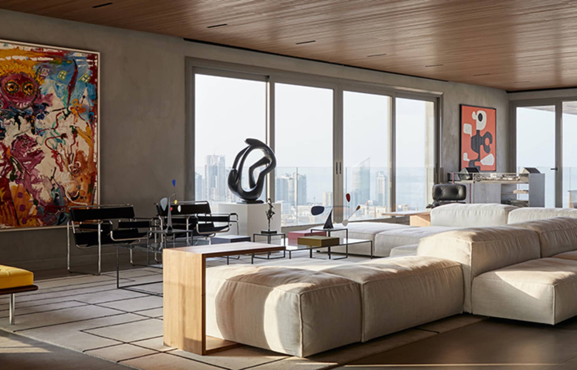 A contemporary living room featuring a concrete floor, large windows, white sectional sofa, and colorful abstract art.