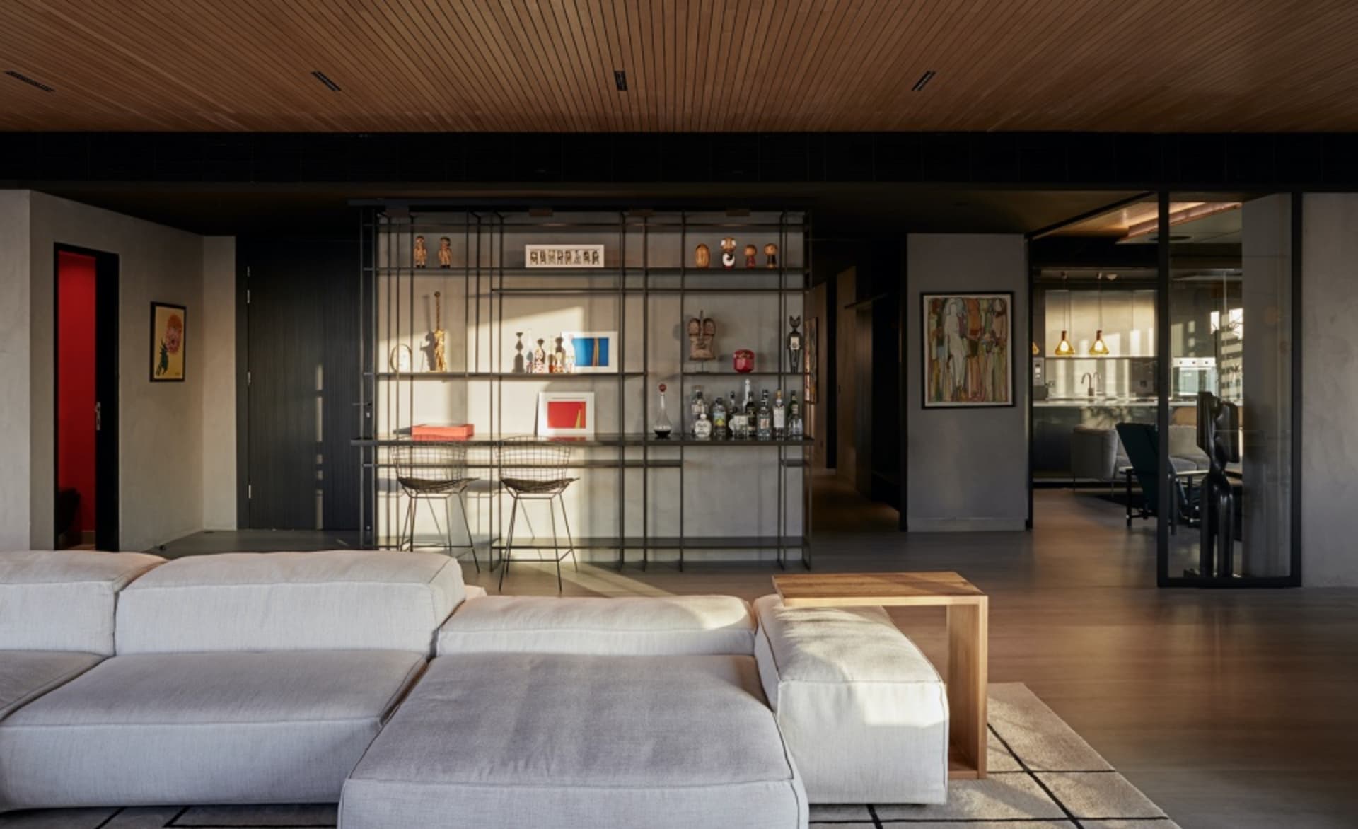 A modern living room featuring a bar area with metal and glass shelves, containing various decorative items, and a wooden cof