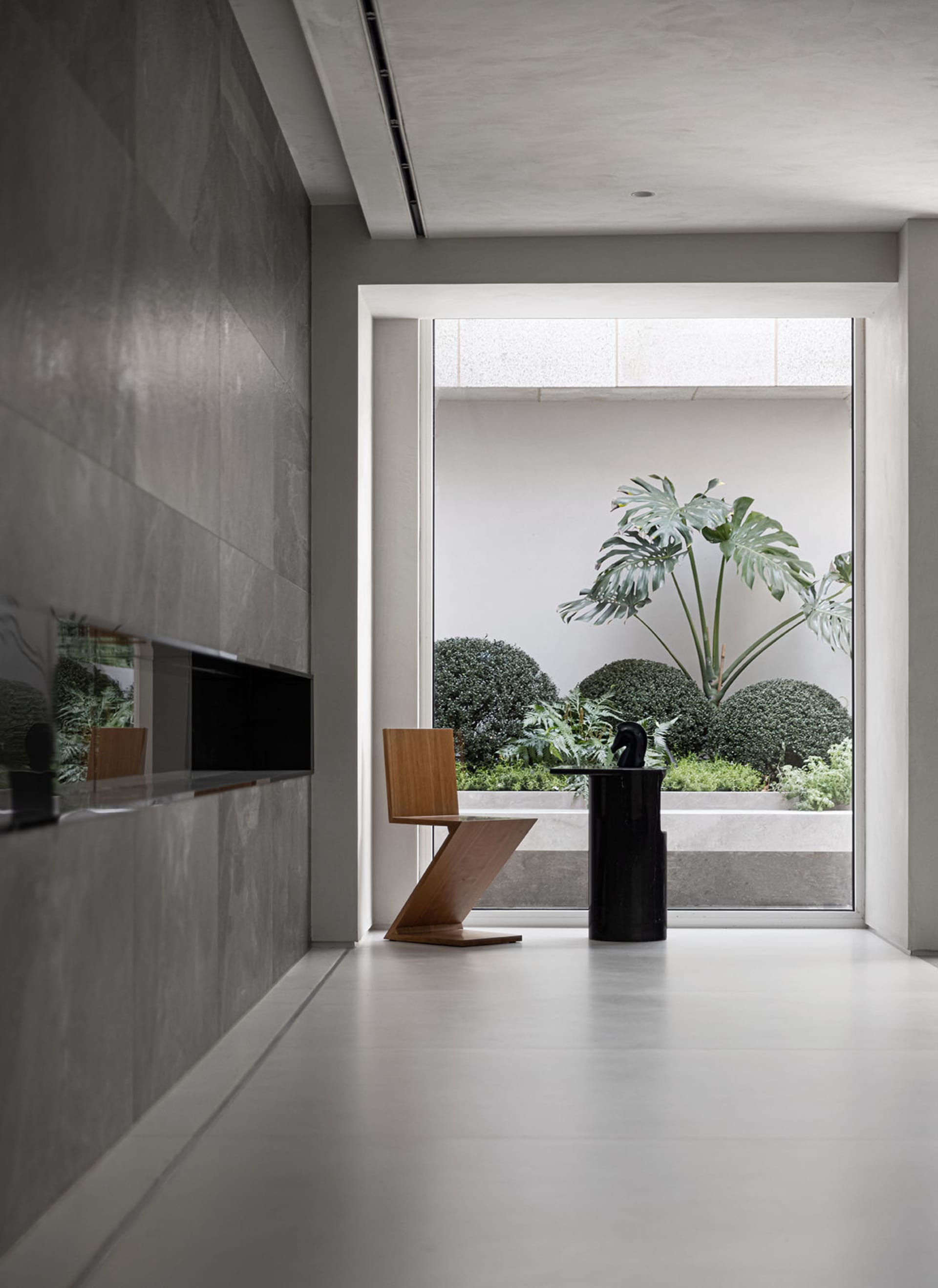 A modern lobby interior with a concrete floor, minimalist furniture, and a view of a green courtyard.