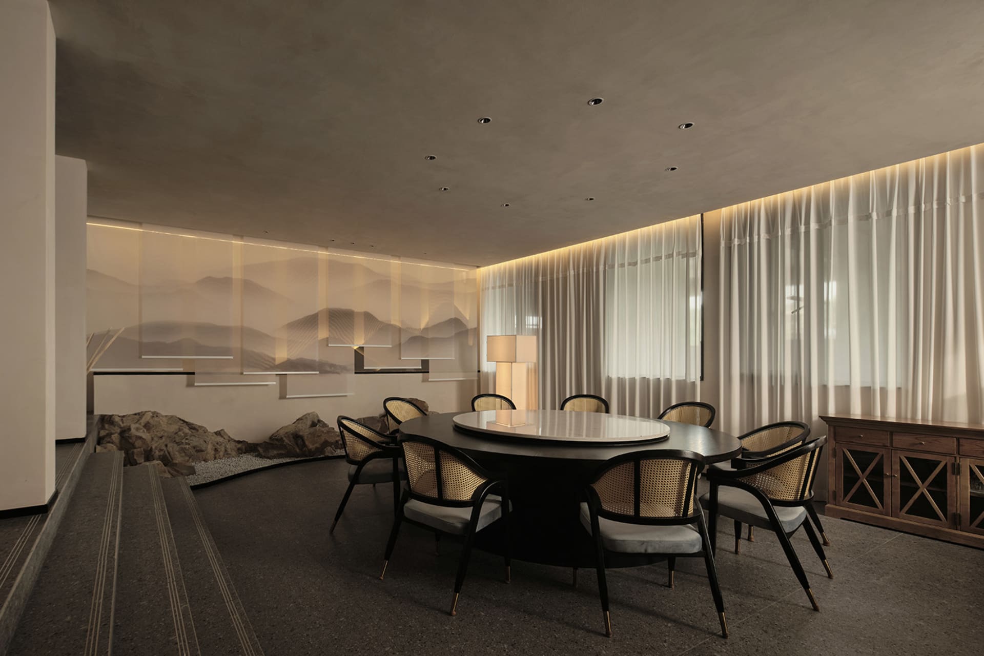 Modern dining room with concrete elements and a round dining table surrounded by black and gold chairs.