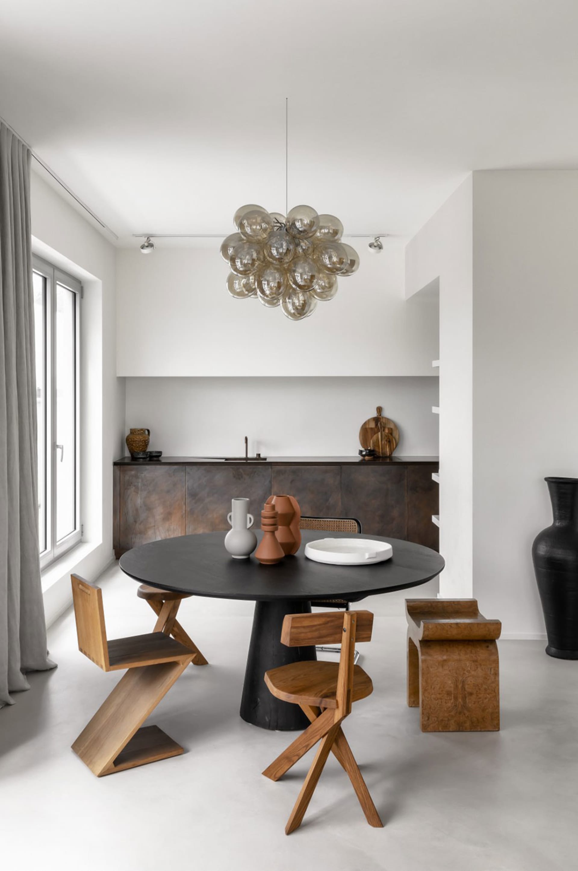 Modern minimalist kitchen with a round black table, wooden chairs, and a cluster of bubble chandelier