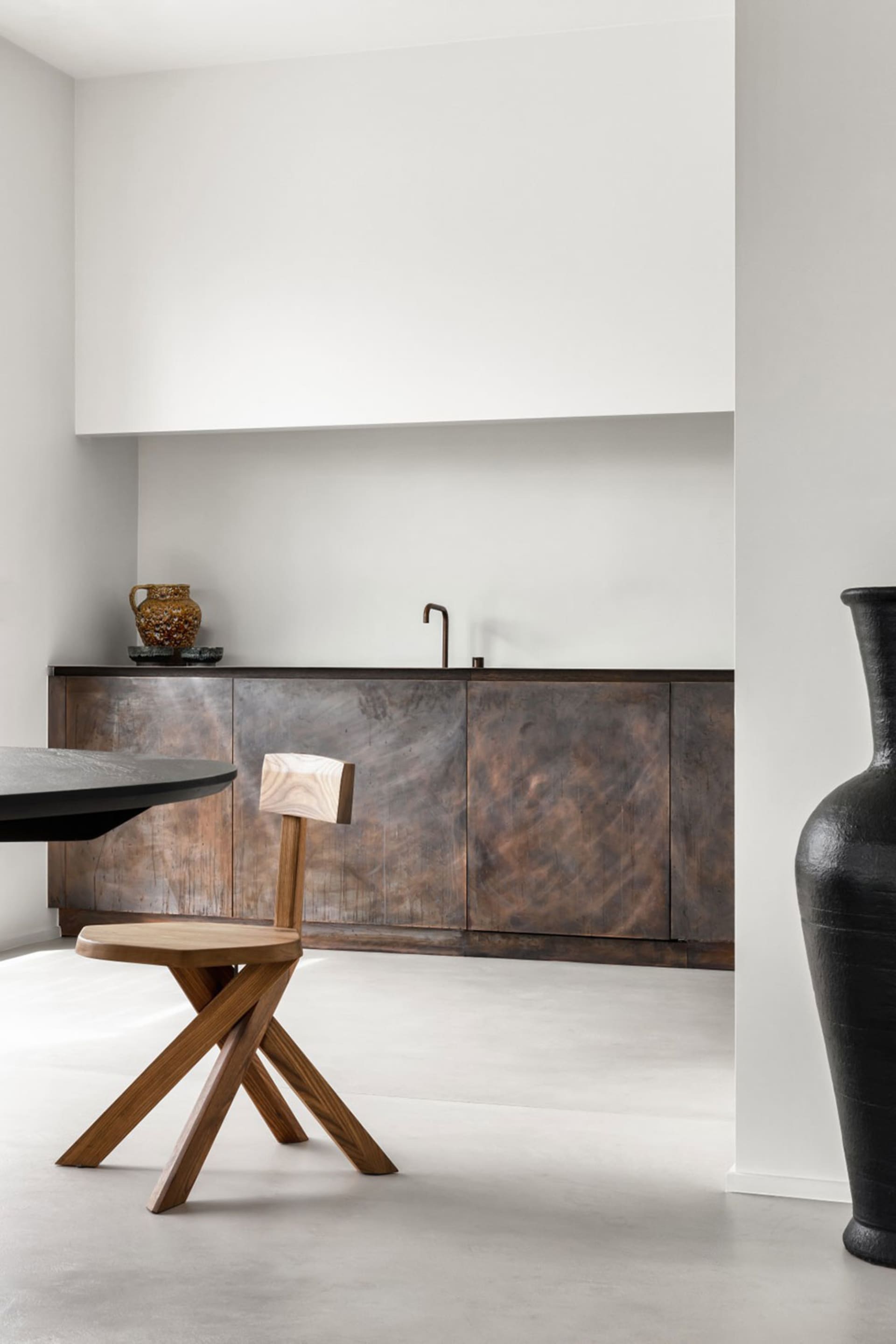 A modern kitchen with metallic wood cabinets and a black table with a wooden stool.