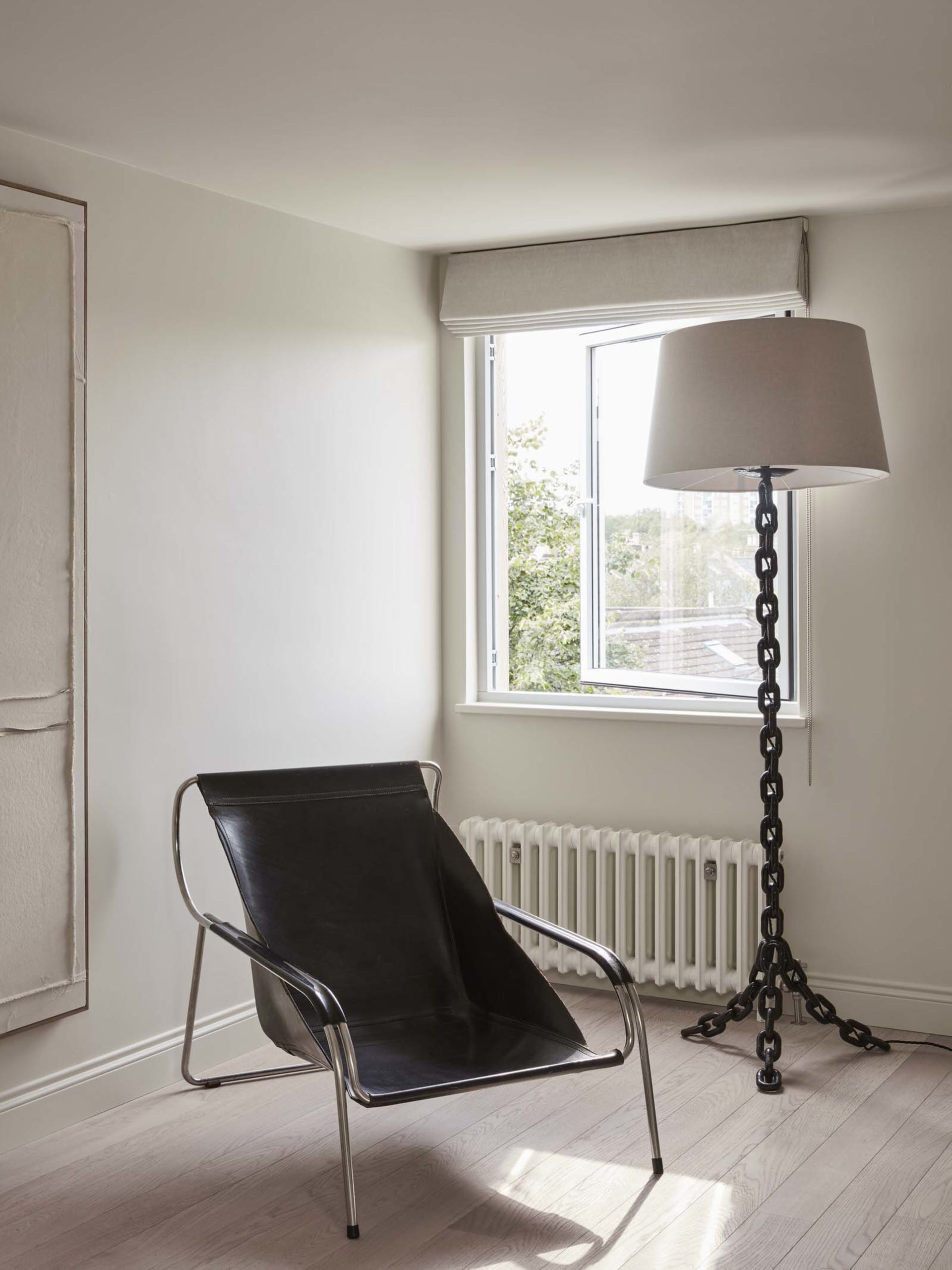 A minimalist living space featuring a black leather lounge chair, metallic chain lamp, and white floor plan.