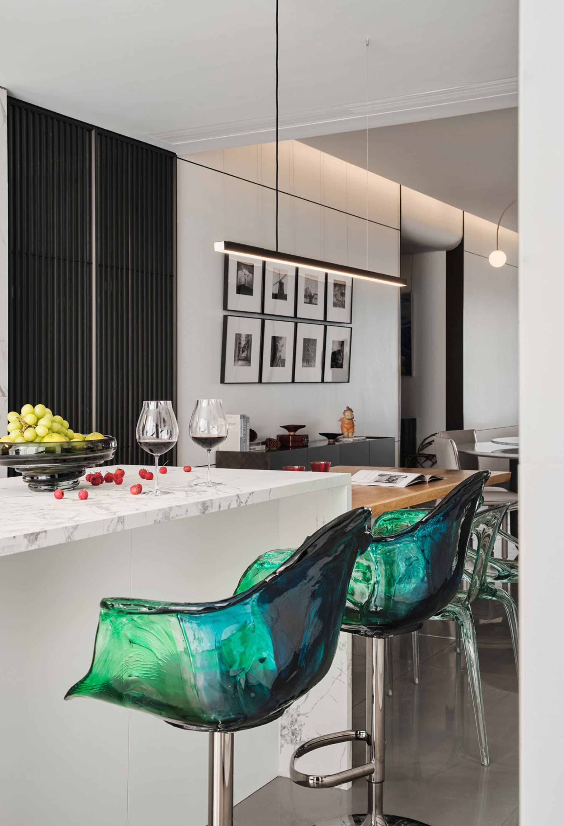 A modern kitchen featuring a marble countertop with green and blue glass bar stools and wine glasses.