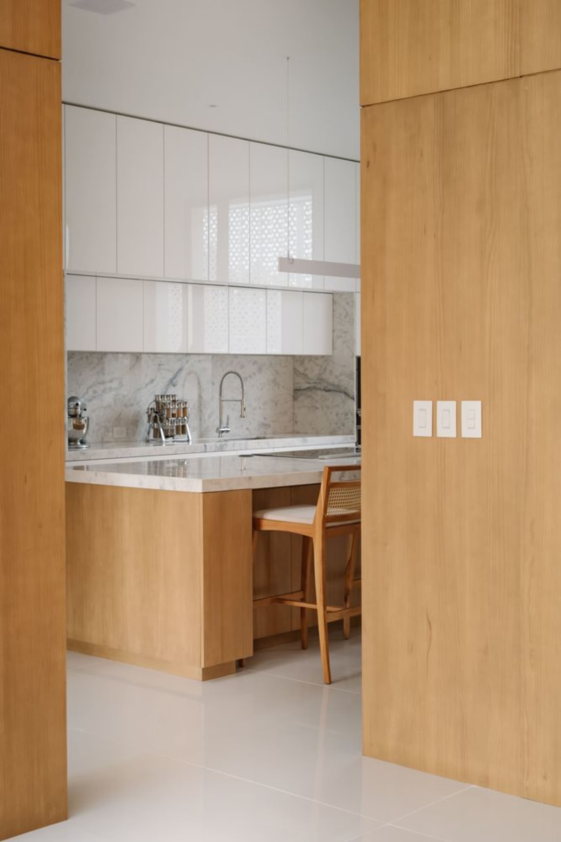 Modern kitchen featuring white marble countertops and backsplash with wooden cabinets and flooring.