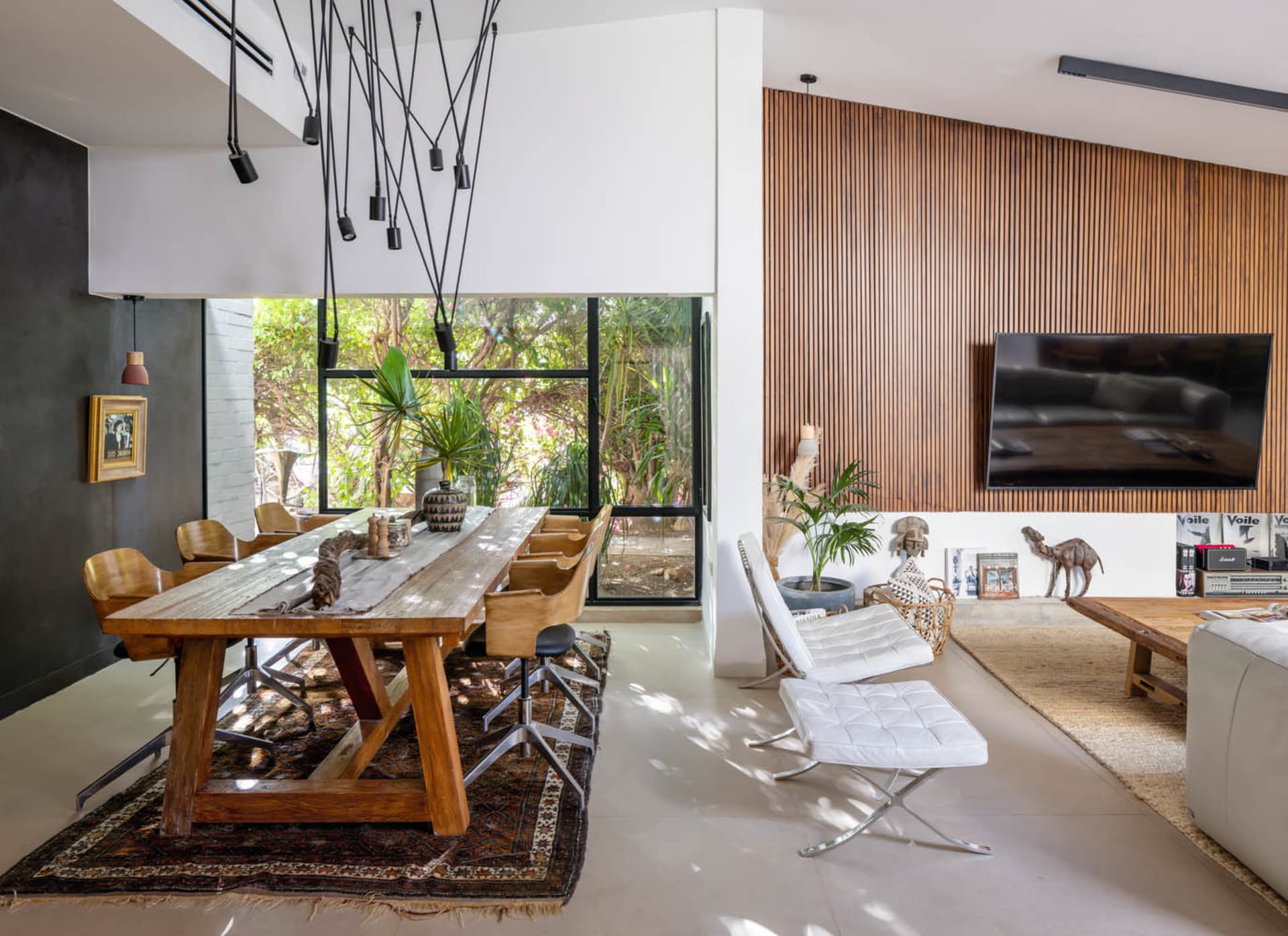 Modern living room featuring a wood-paneled wall and large windows showcasing a green outdoor space.