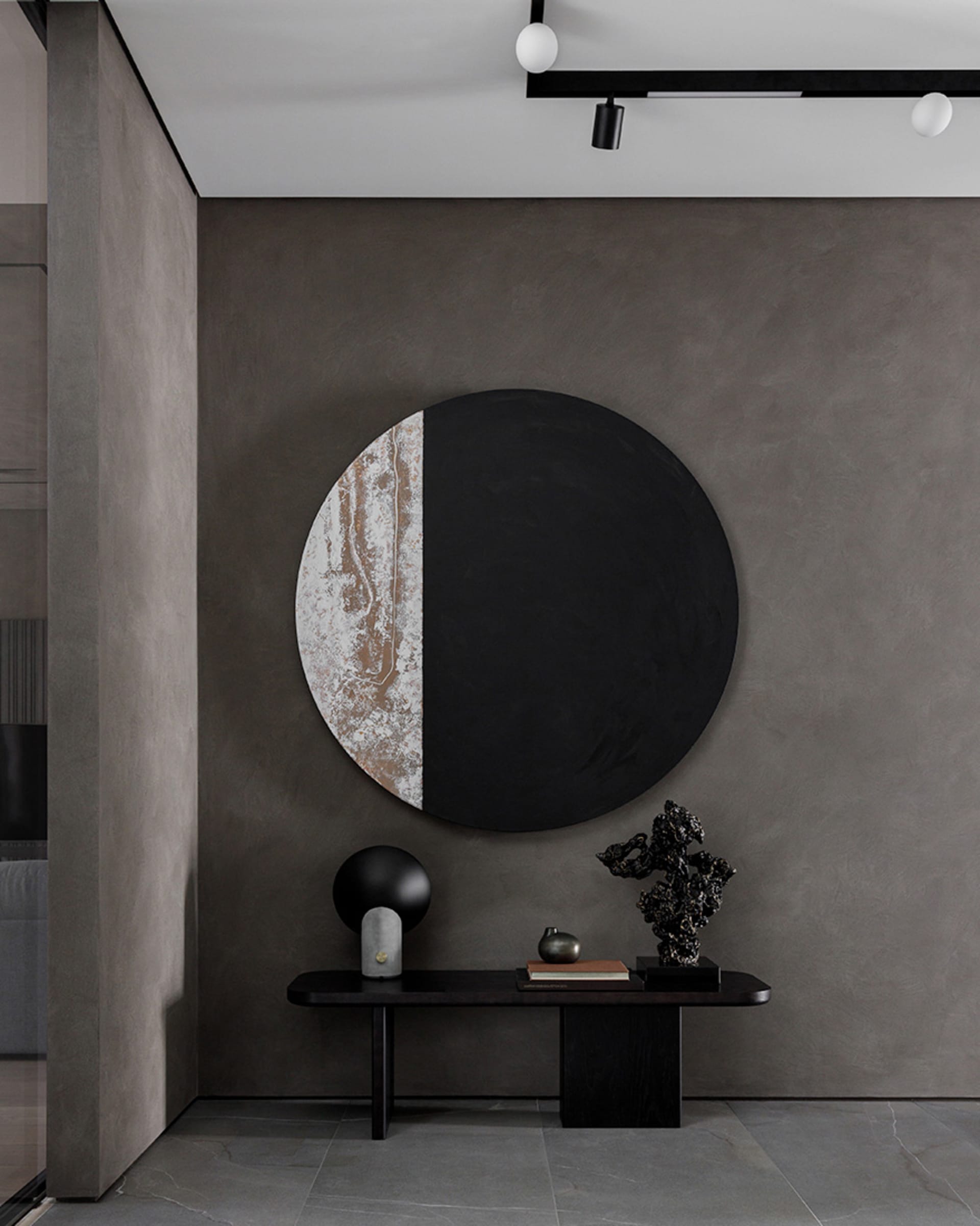 A minimalist entrance lobby featuring a metal table with various decorative items and a large circular artwork with a black a