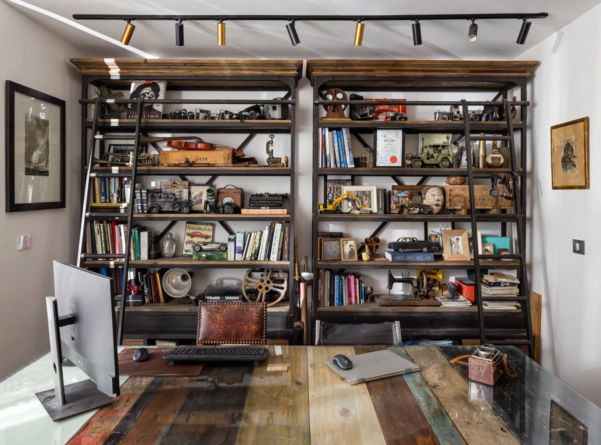 A home office with wooden shelves filled with books, cameras, and vintage items.