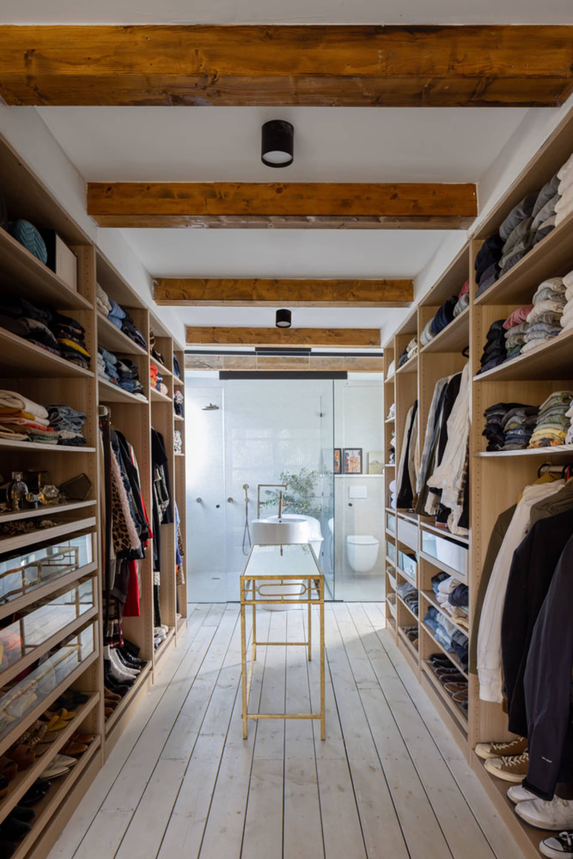A modern closet with white wooden shelves, metal furniture, and a glass bathroom door.