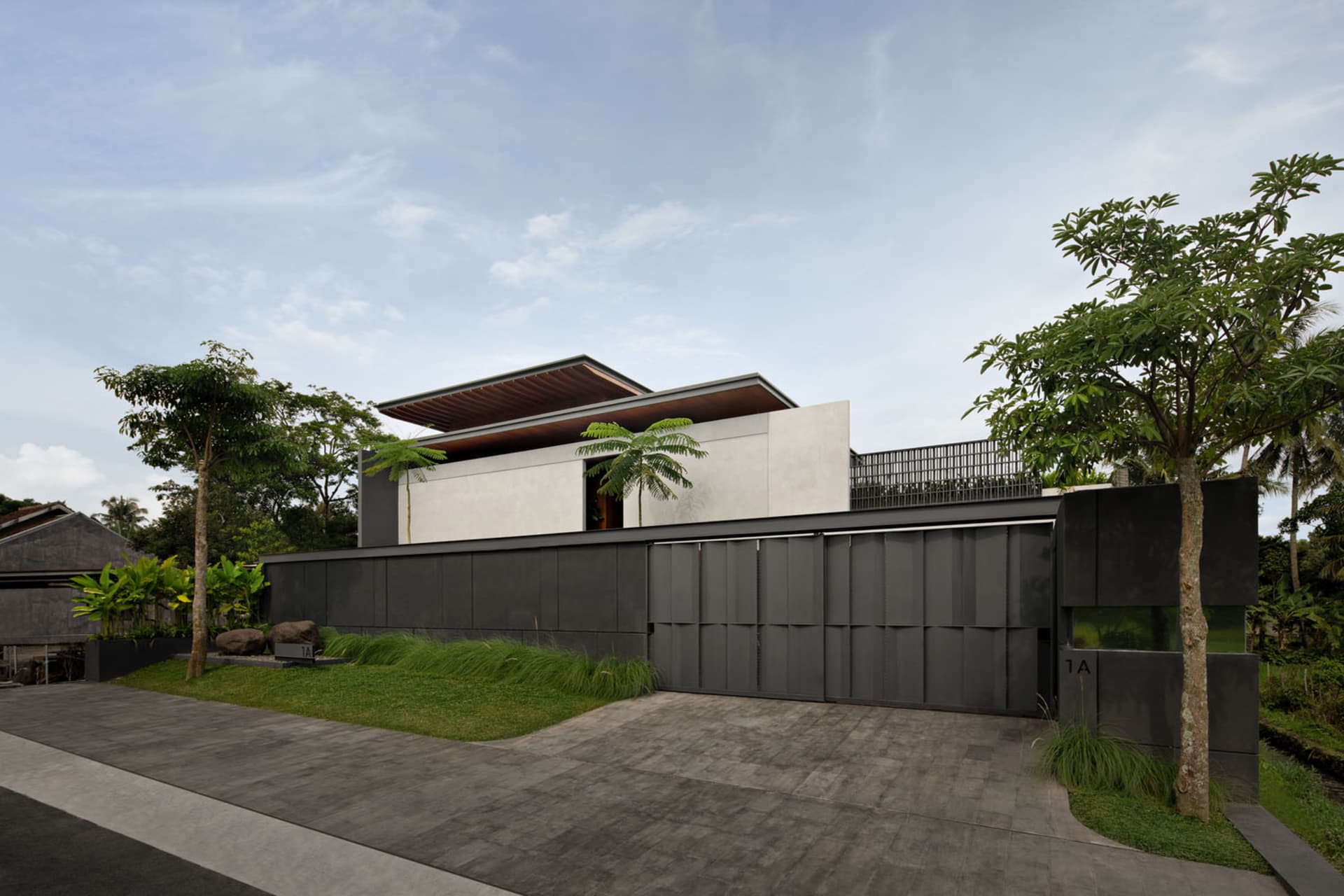 A modern, minimalist concrete house with a flat roof and large windows, featuring a sleek black entrance and surrounded by gr